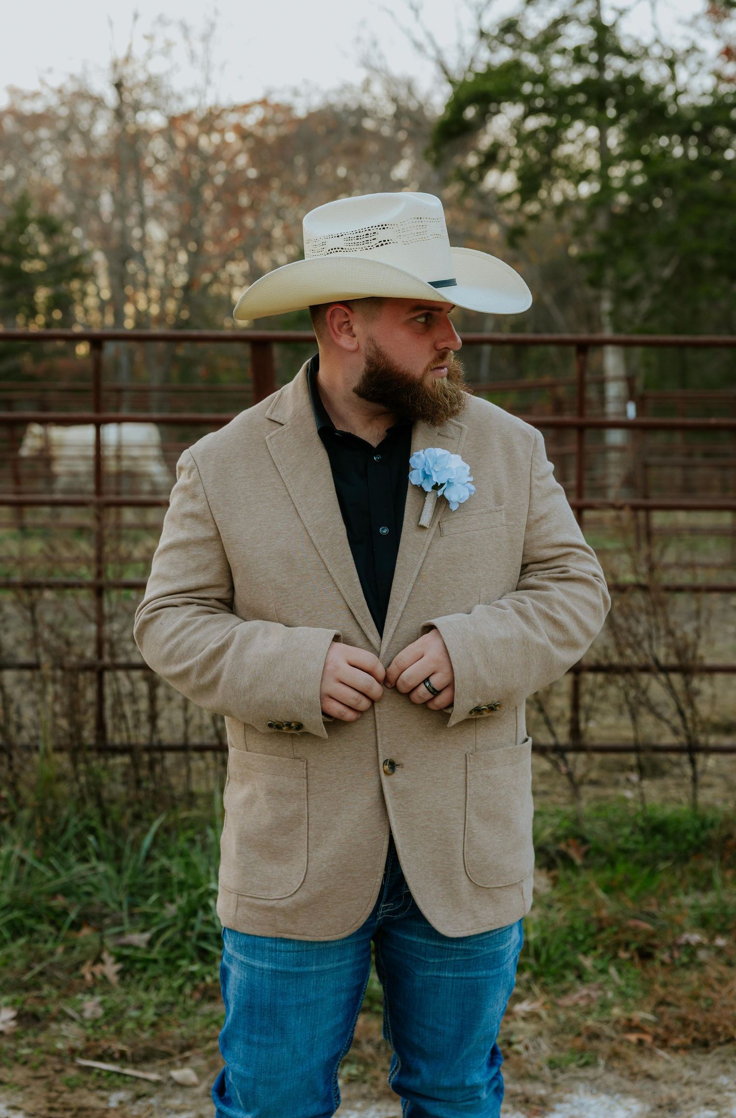 A person in a beige blazer and cowboy hat poses against a rustic fence background.
