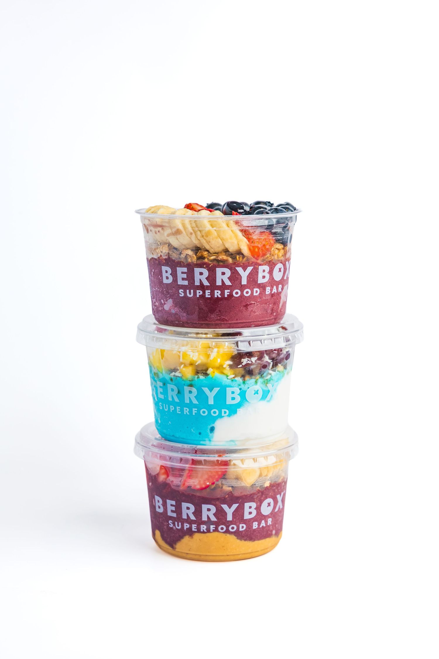 Three stacked BerryBox Superfood Bar cups filled with colorful acai bowls and fresh toppings on white background.