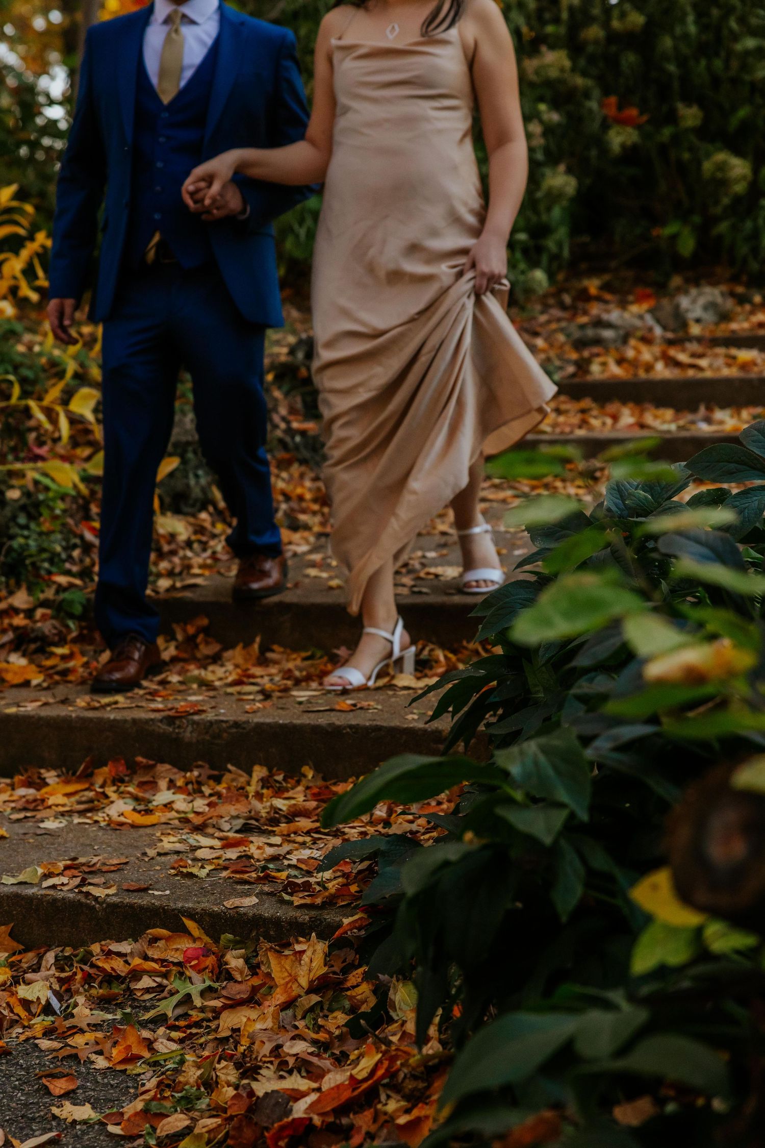 Engagement couple's feet and dress hem surrounded by scattered autumn leaves on stone steps at Lafayette Park in St. Louis.