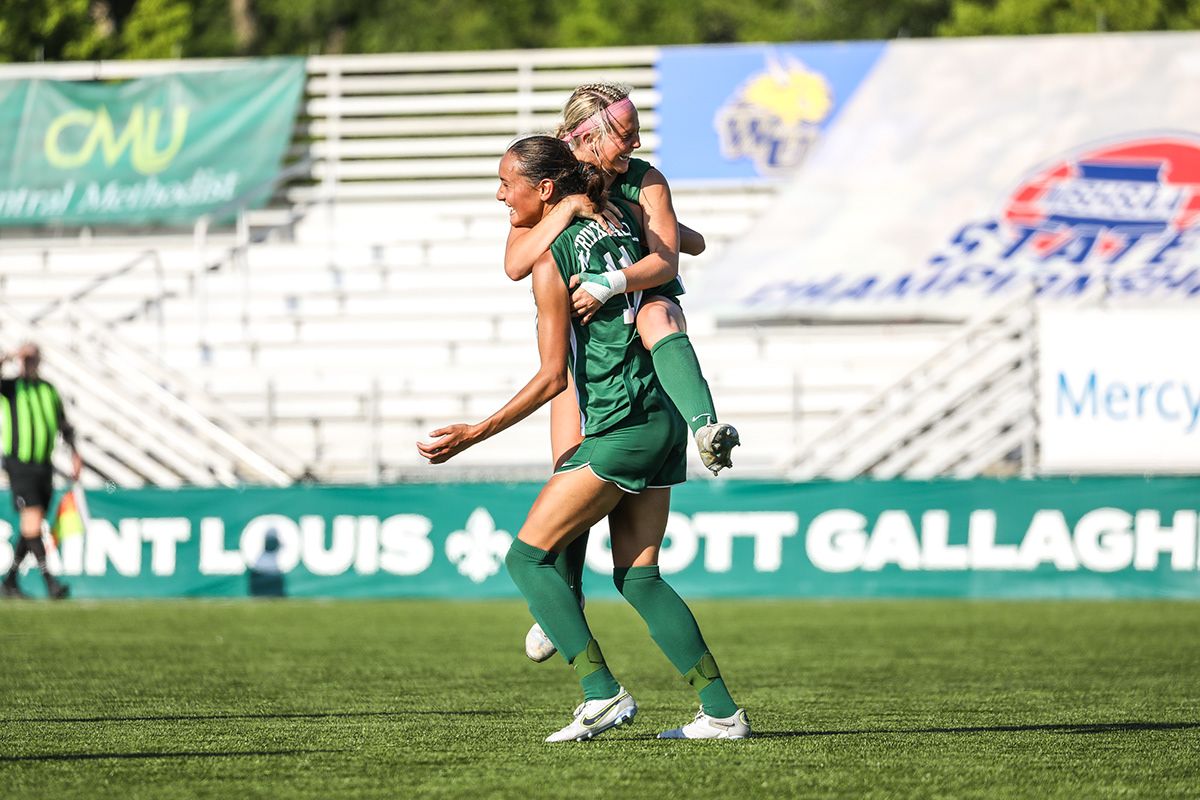 Soccer players in green uniforms running on professional sports field during match.