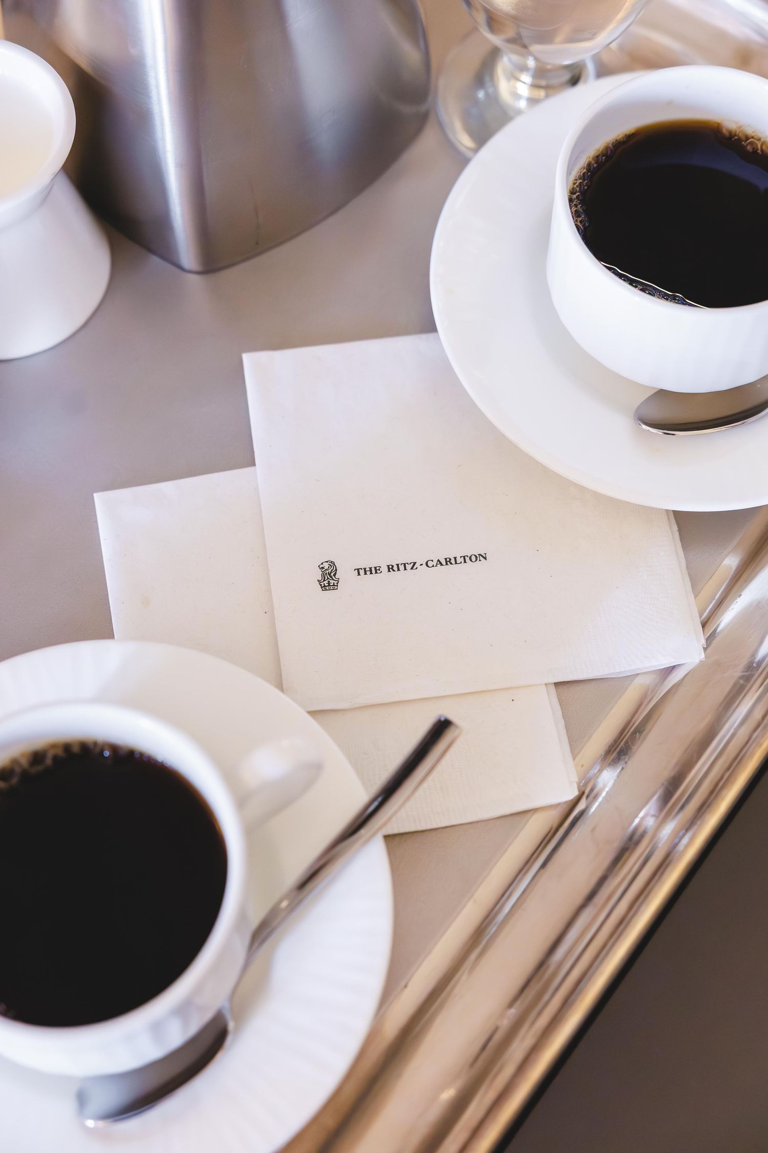 Two cups of black coffee served on white saucers with a Ritz-Carlton branded notecard on a silver tray.