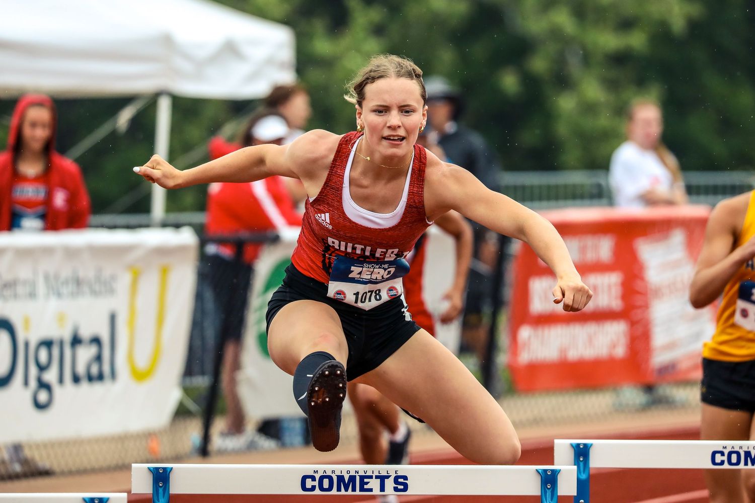 Track athlete clearing hurdle during competitive race.