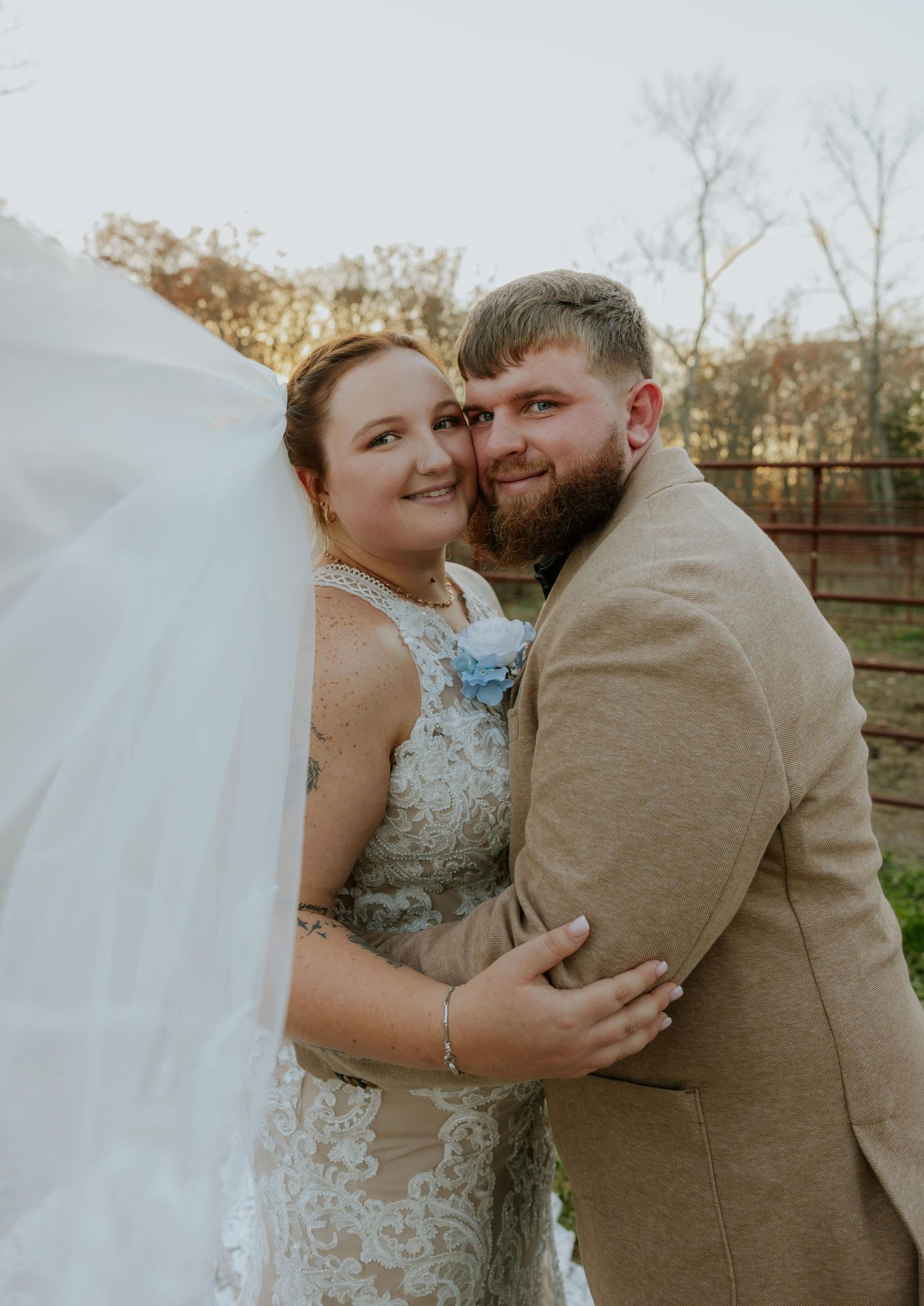 A couple shares an intimate moment in wedding attire against a rustic outdoor backdrop.