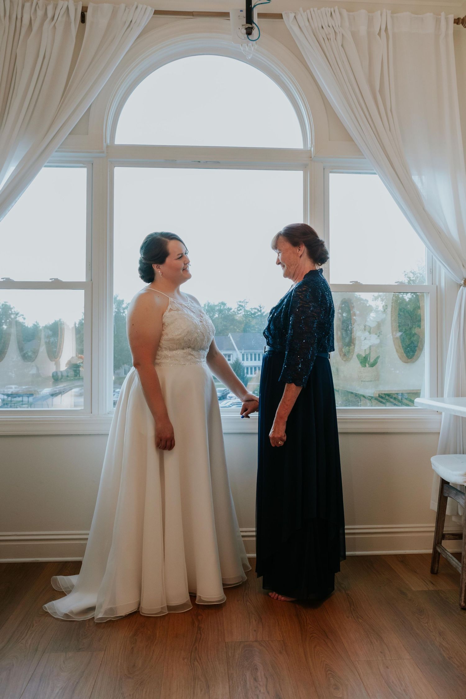 Bride and mother share a joyful moment in an elegant room with large windows and hardwood floors for the wedding in St. Louis.