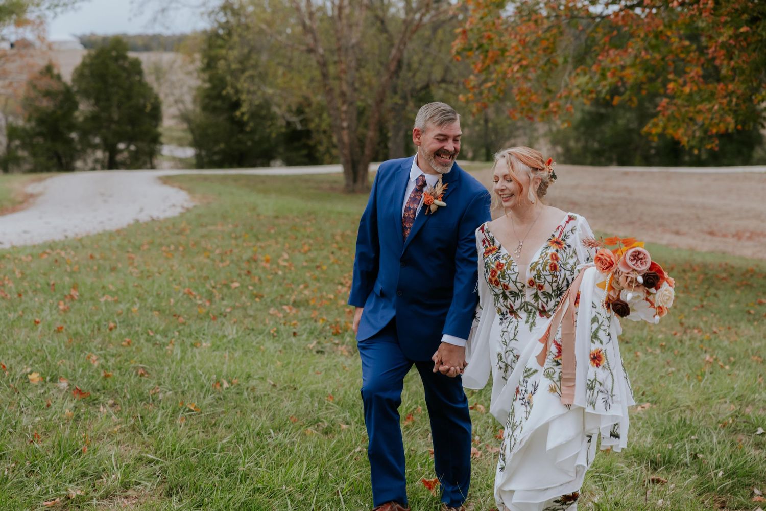 Newlyweds embrace in a fall outdoor setting with orange and burgundy florals.