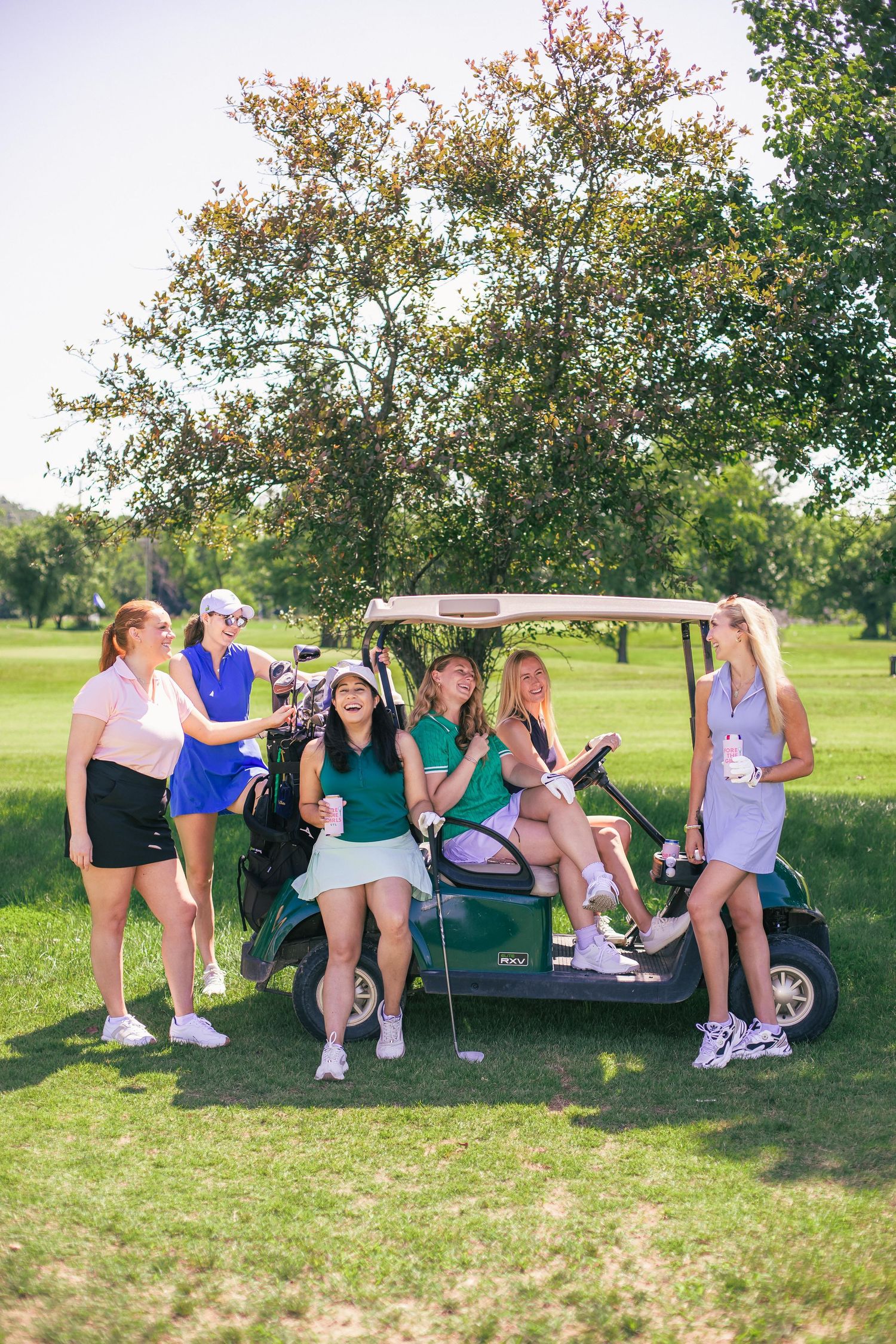 Group relaxing under a golf cart canopy on a sunny day at a golf course in St. Louis.