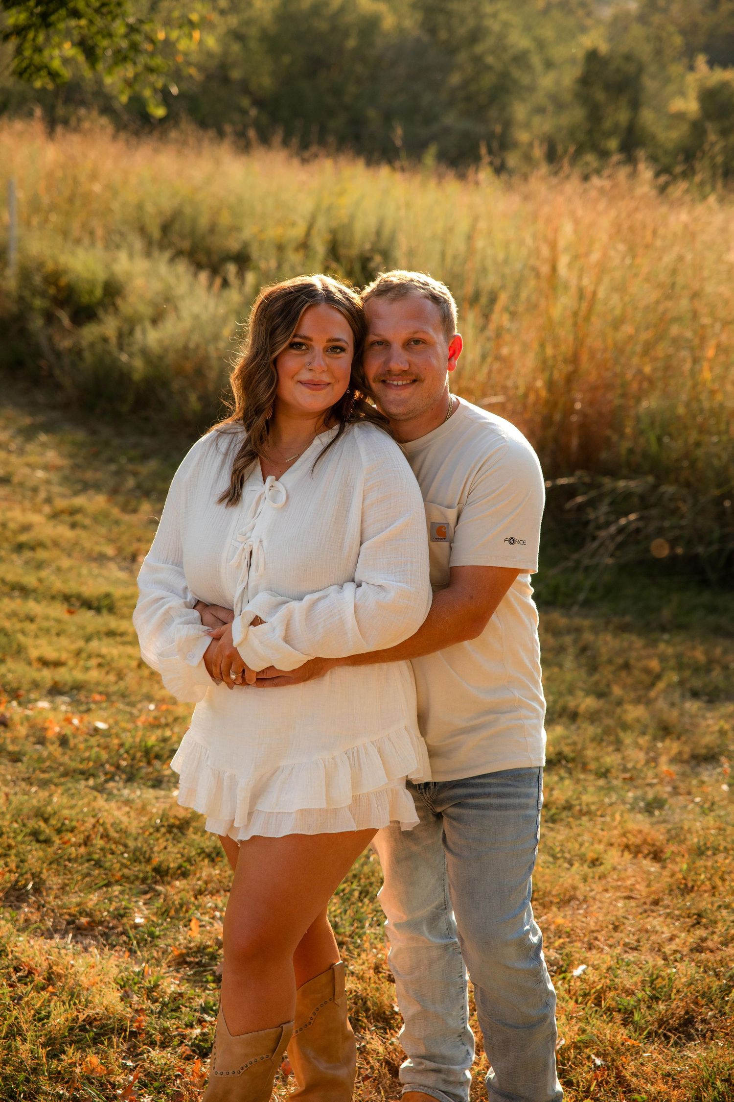 A couple embraces in a golden sunlit field during autumn at Queeny Park in St. Louis.