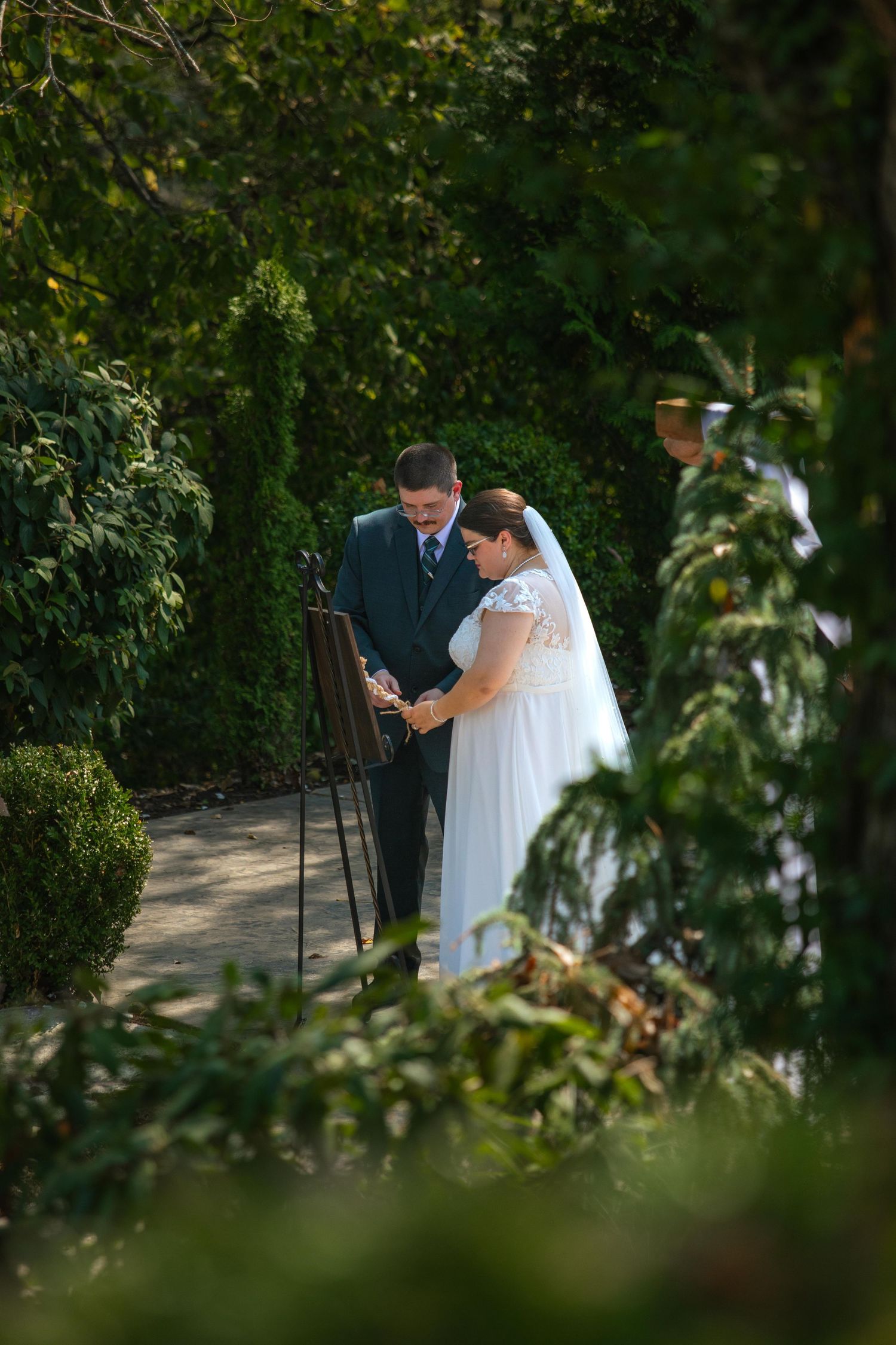 Wedding ceremony moment captured through foliage in an outdoor garden setting in St. Charles, Missouri.