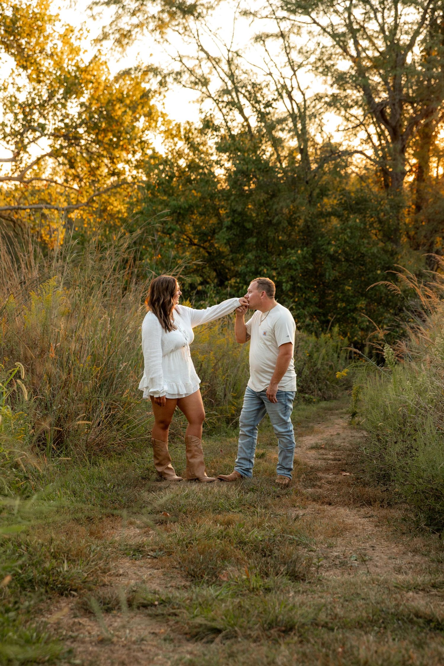 Couple in casual attire walking and posing playfully on a nature trail during golden hour at Queeny Park near St. Louis.