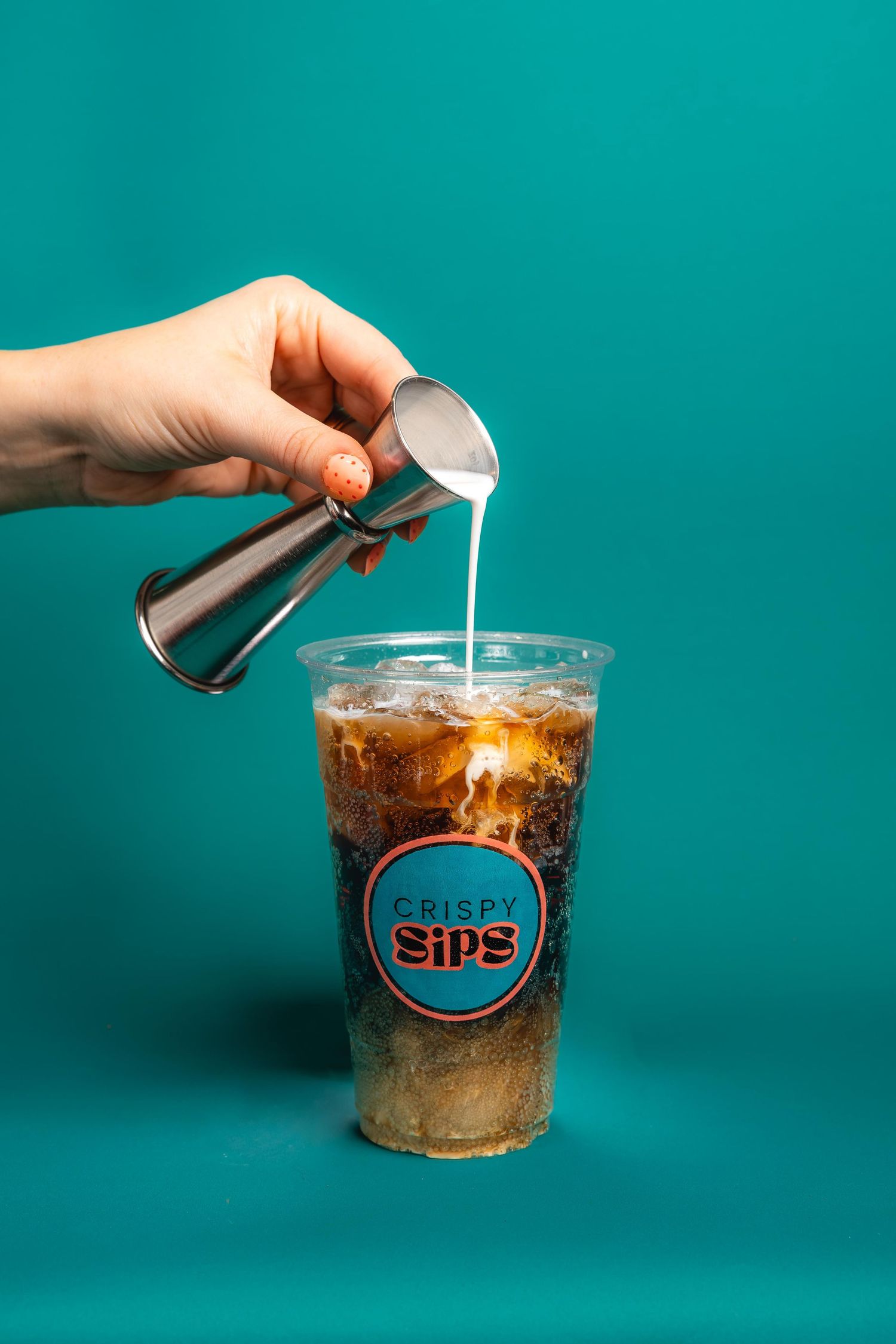 Hand pouring cream into iced coffee against turquoise background in sequence of four progressive shots.