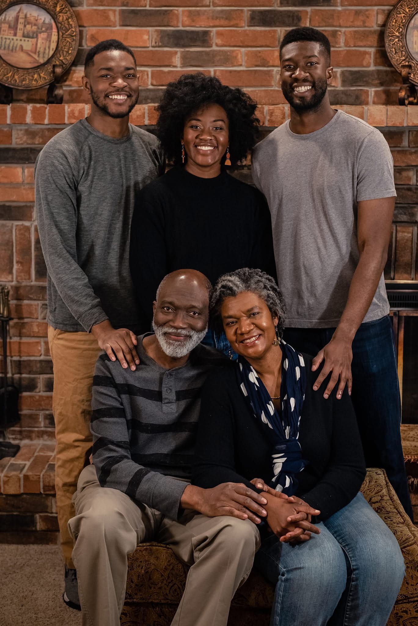 A multi-generational family portrait session against a rustic brick wall backdrop showing warm smiles and connection.