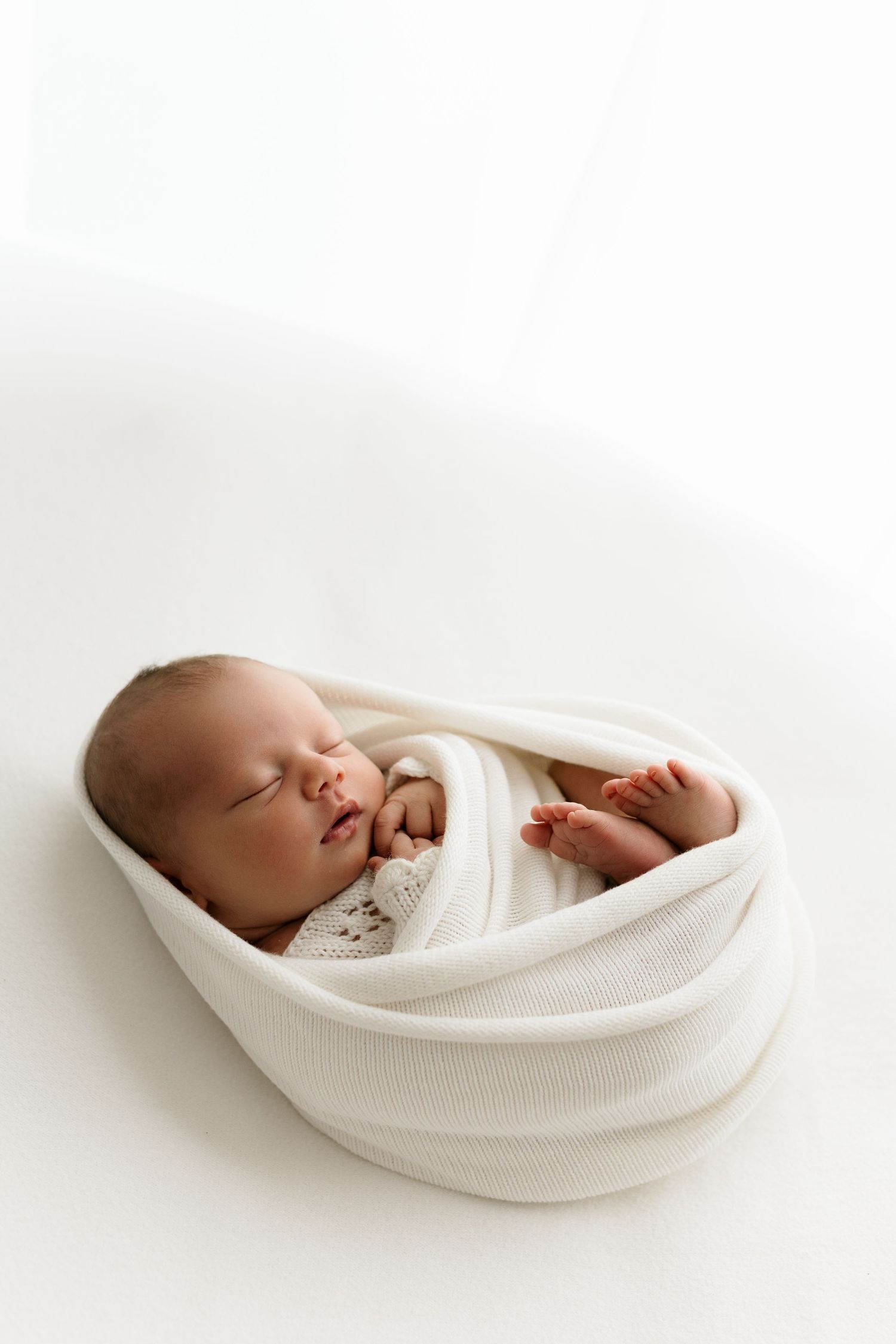 Peaceful newborn baby swaddled in white wrap sleeping on white background.