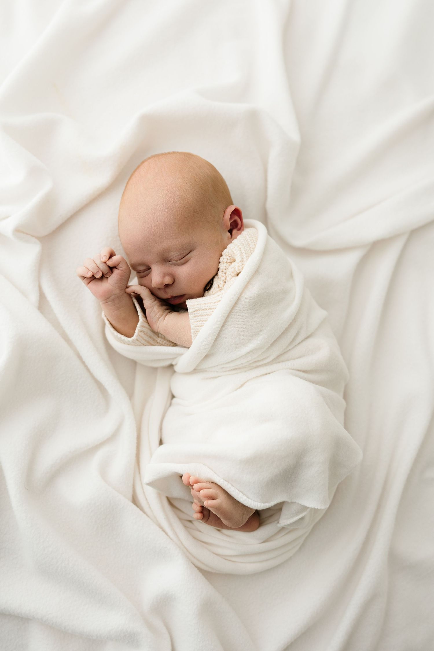 A peaceful sleeping baby wrapped in soft white blankets lies on white bedding in a series of photos.