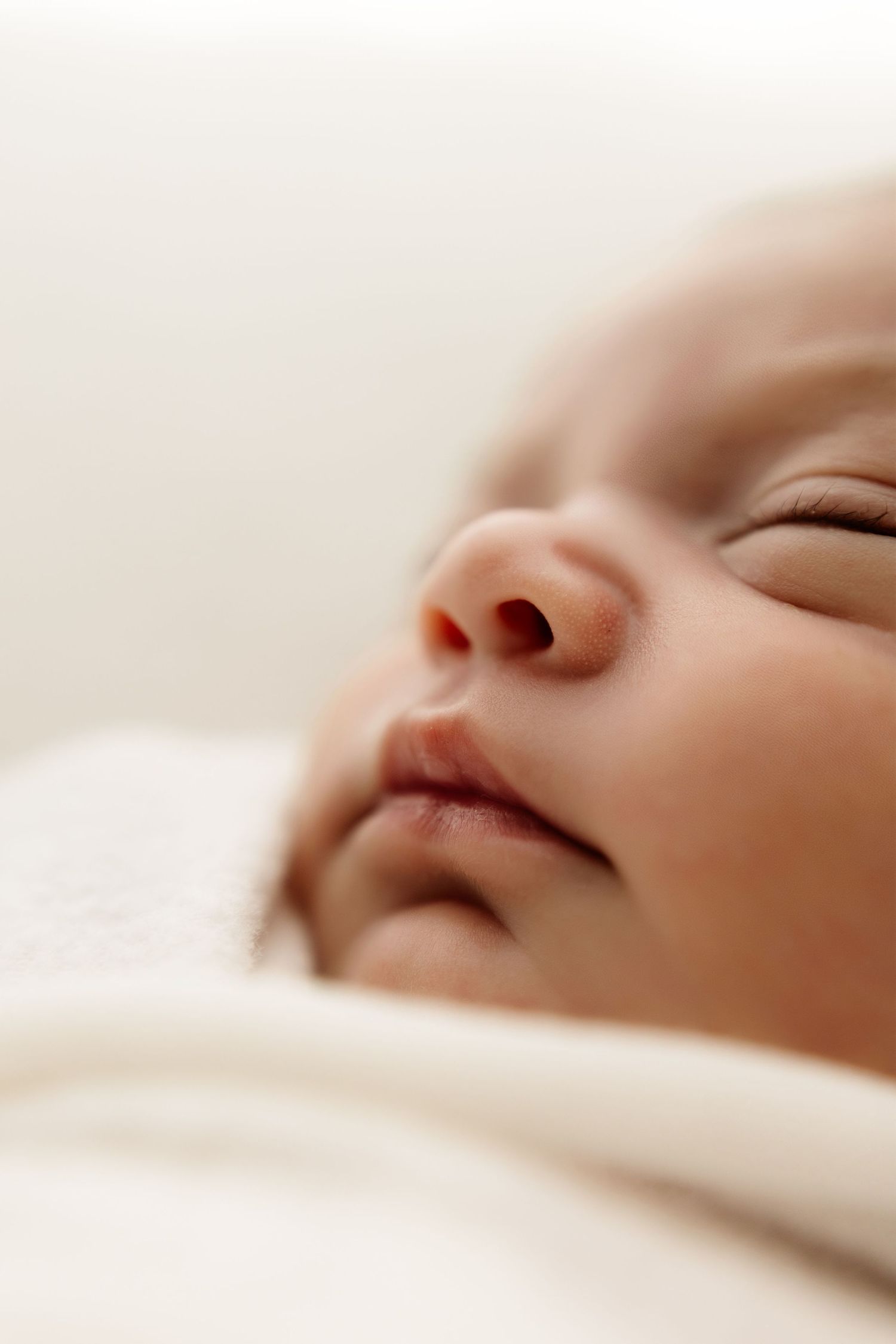 Close-up of a peaceful sleeping newborn baby wrapped in a soft white blanket, with delicate features and smooth skin.