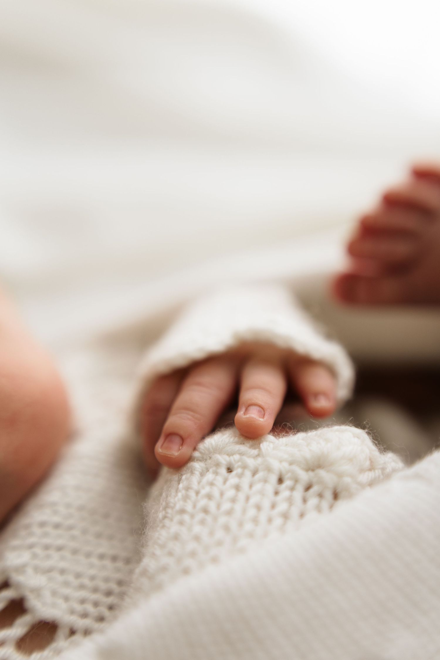 Close-up of a newborn baby's tiny hand resting on a soft white knitted blanket.