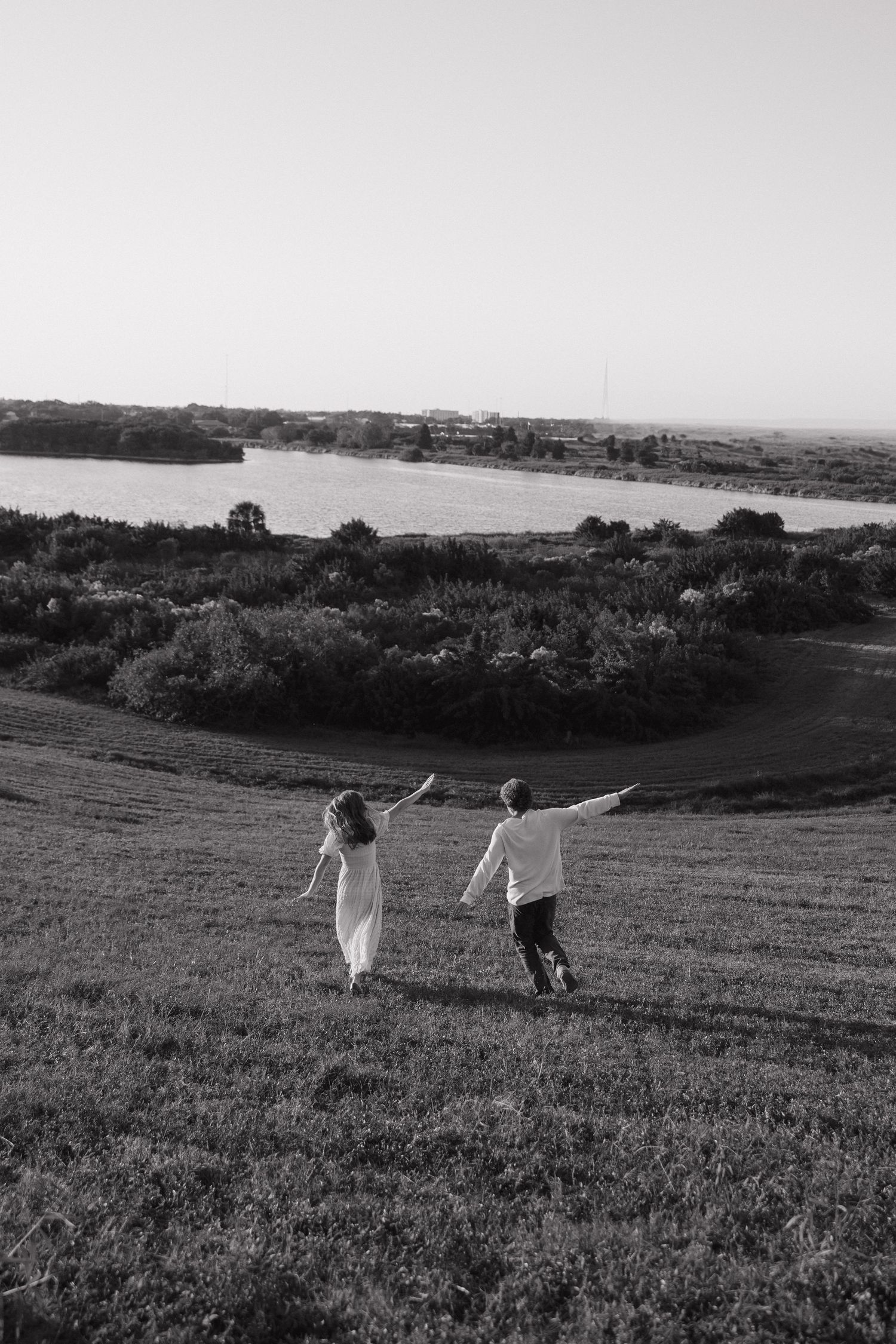 Couple holding hands while walking across grassy field with ocean view.
