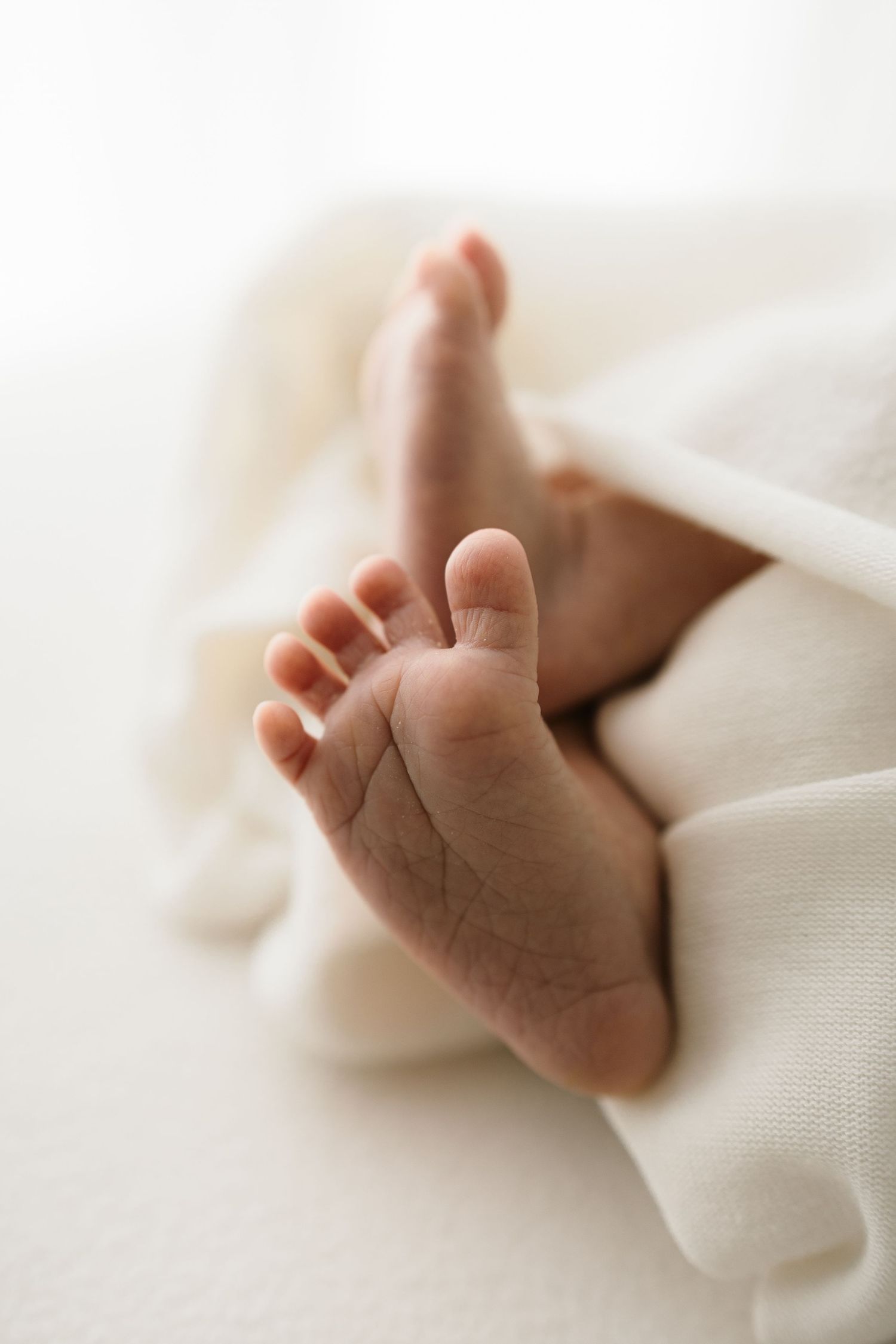 Tiny baby feet peek out from soft white fabric in a tender newborn photography pose.