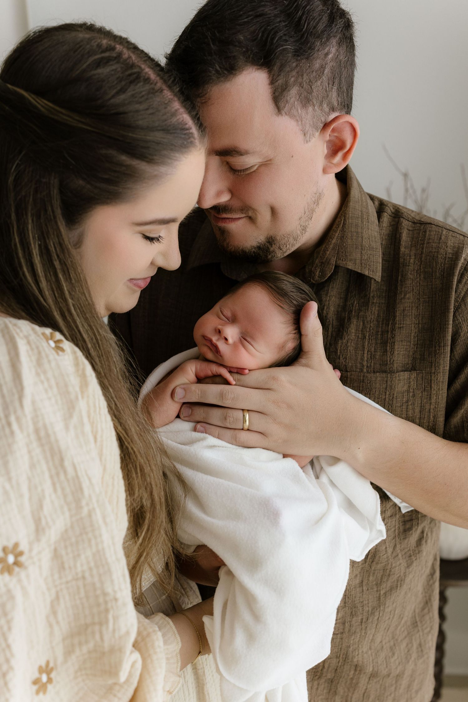 New parents tenderly gaze at their sleeping newborn baby wrapped in white, sharing a precious family moment.