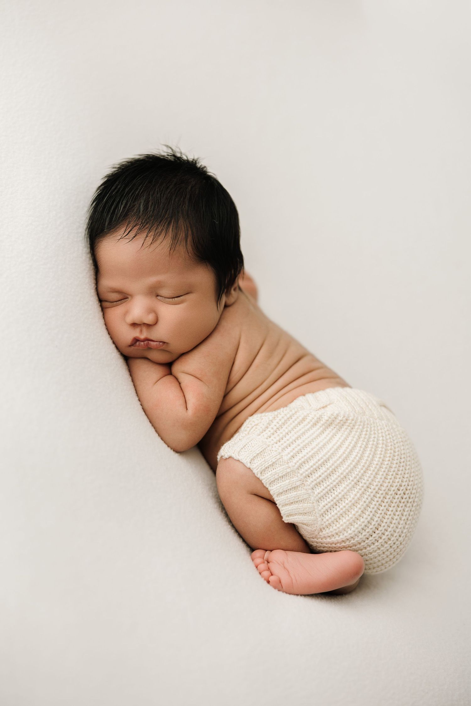 A series of three minimalist black and white photos showing a sleeping newborn baby in soft knit wrapping.