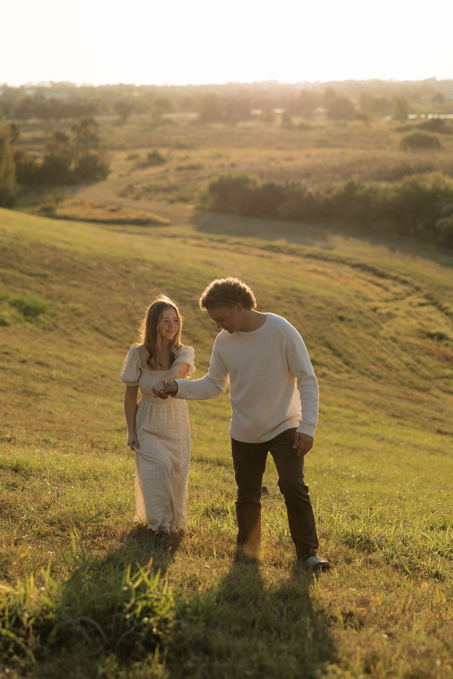 Couple walking together on scenic hillside during golden hour.