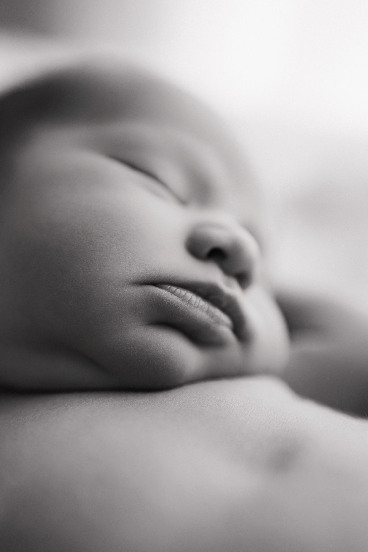Black and white close-up photo of a peaceful sleeping newborn baby with soft, delicate features.