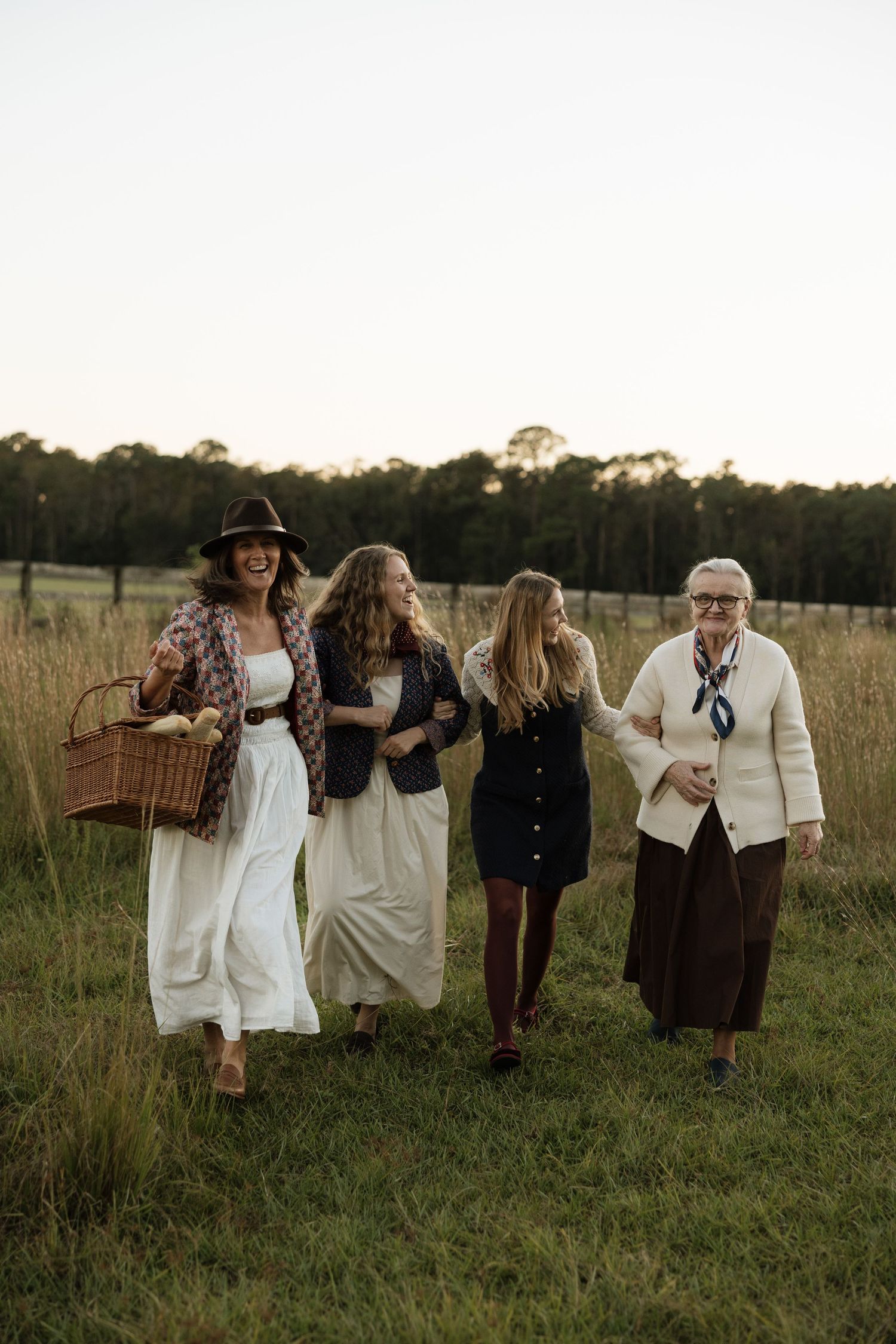 Group of people in light colored clothing walking together through tall grass at sunset.