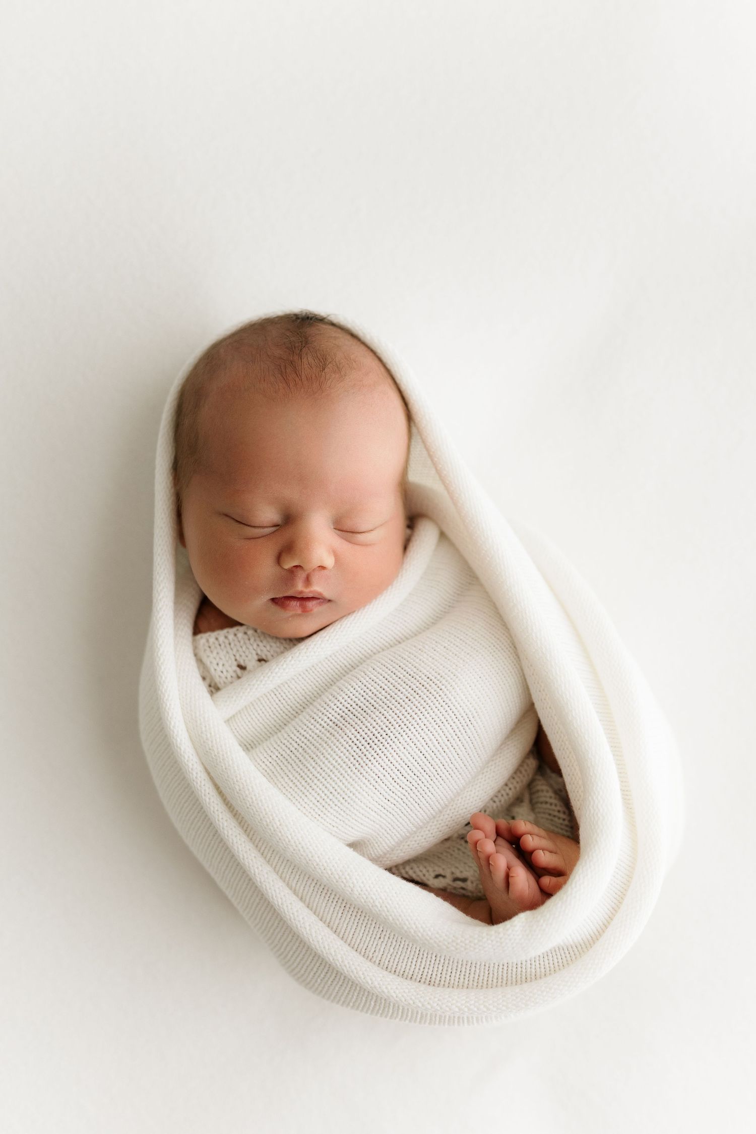 Sleeping newborn baby swaddled in white wrap on white background, peaceful infant portrait photography.