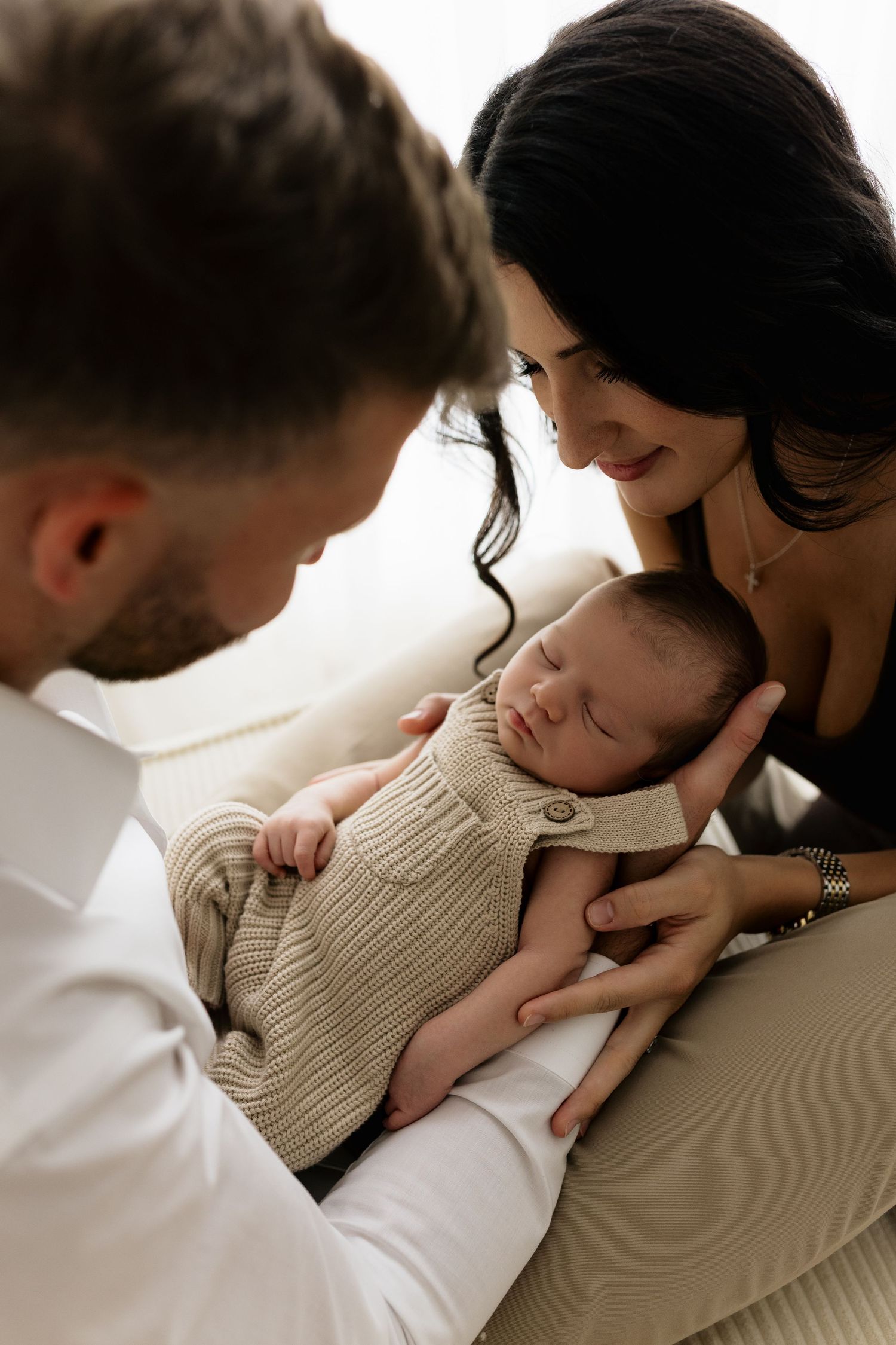 Loving parents admiring their sleeping newborn baby dressed in a cozy cream knit outfit.