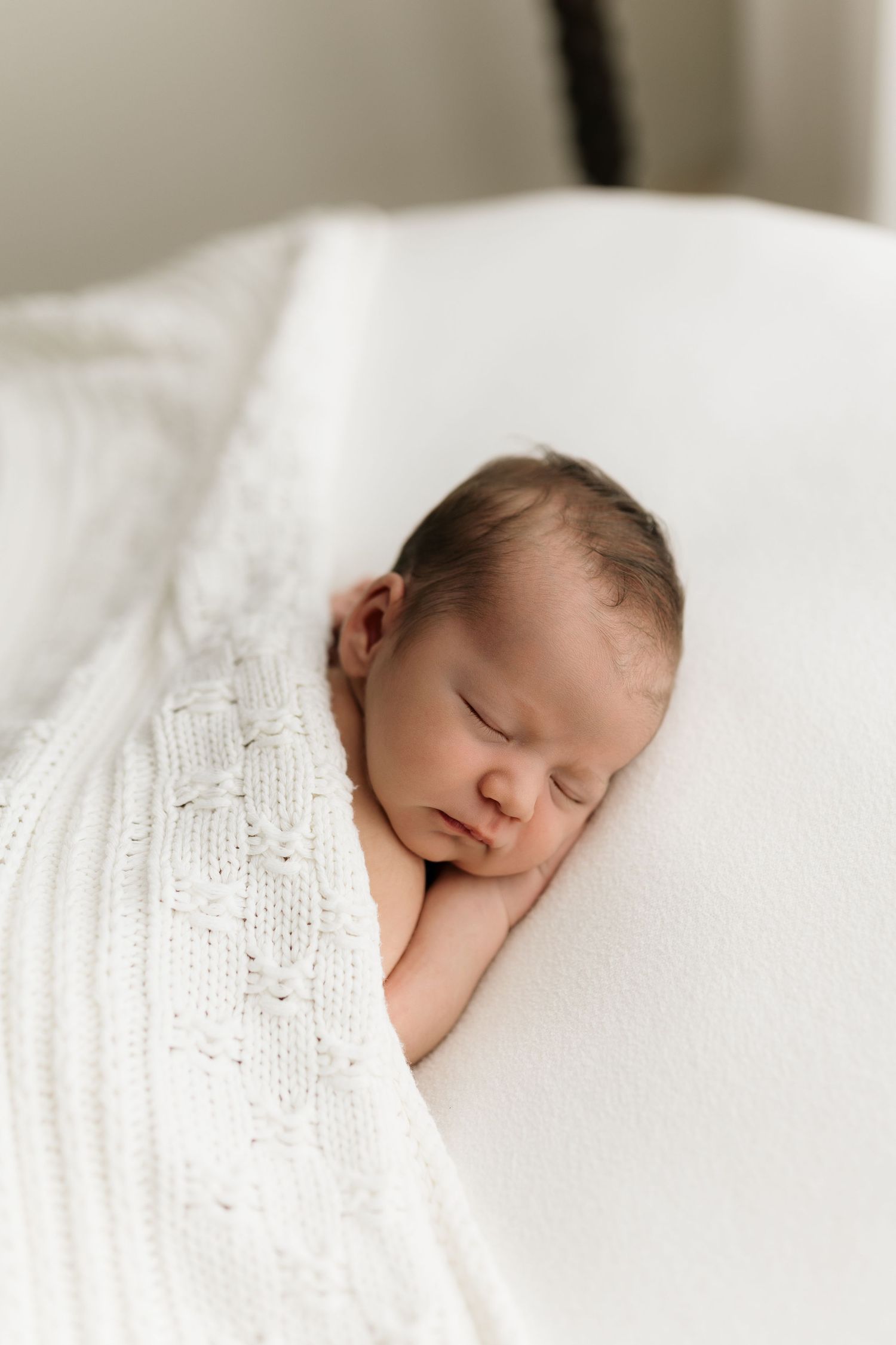 Peaceful newborn baby sleeping wrapped in a soft white knit blanket on a white surface.