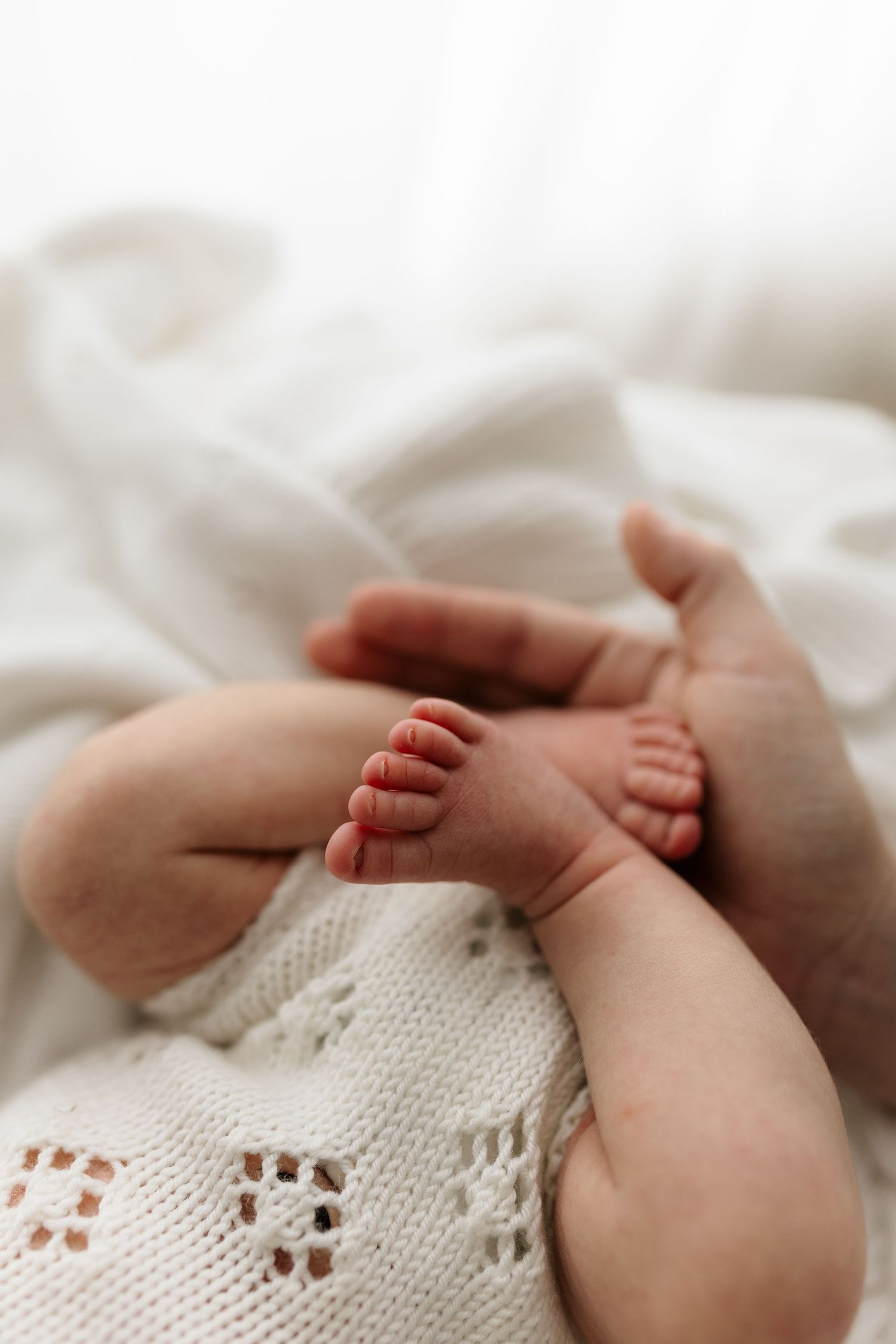 Close-up of tiny newborn baby feet resting on a soft white knit blanket, captured in delicate detail.