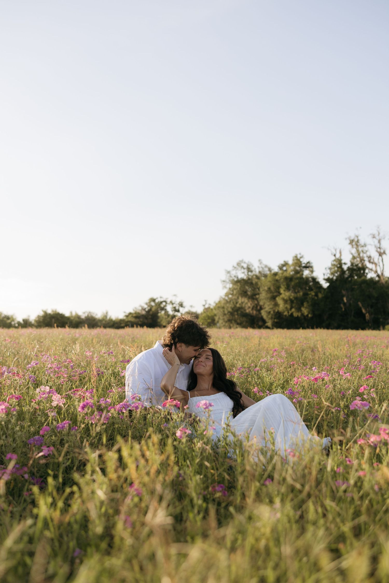 Romantic couple sitting in a blooming wildflower meadow, sharing a tender kiss at golden hour.
