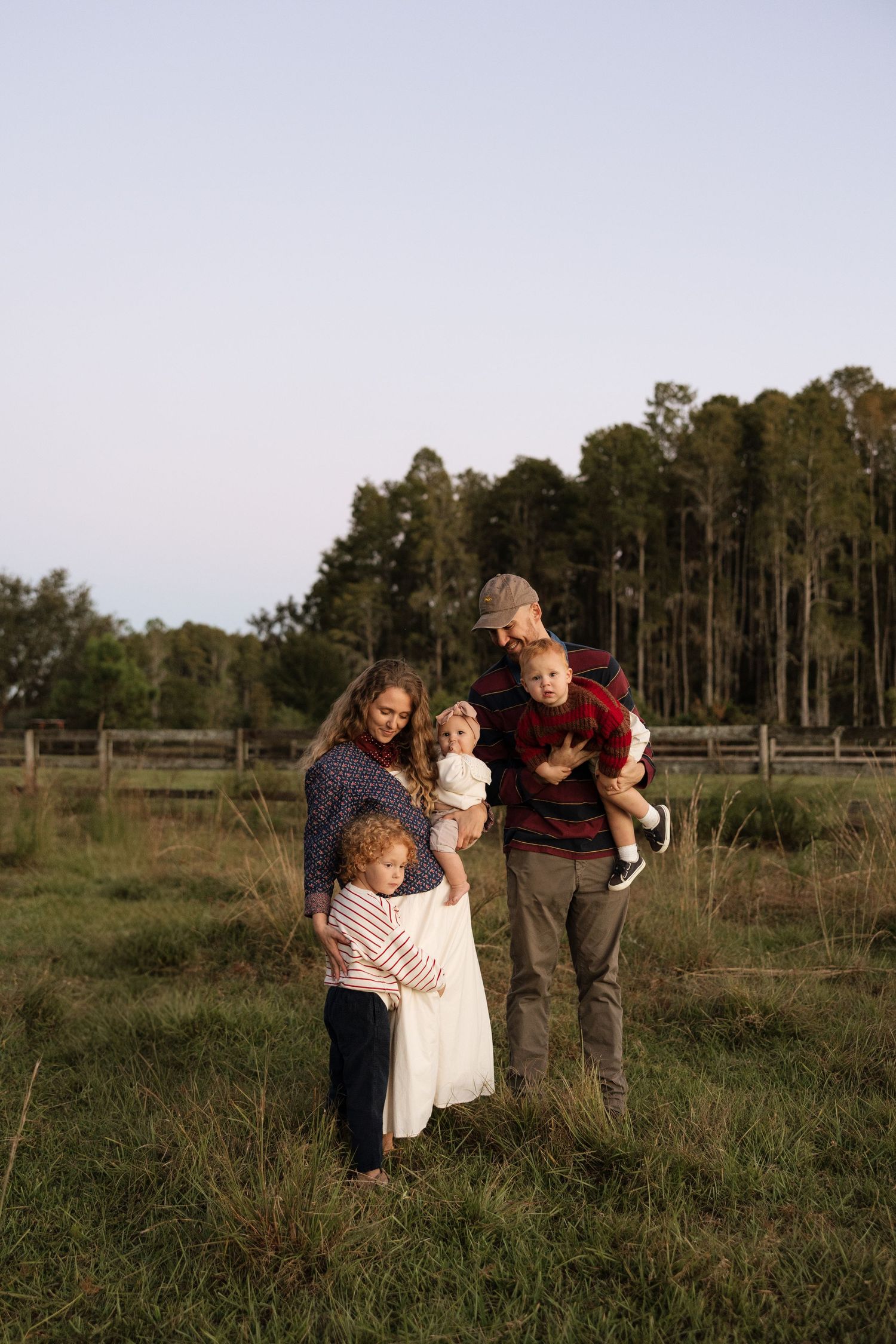 Family gathering in open field during sunset with pine trees in background.