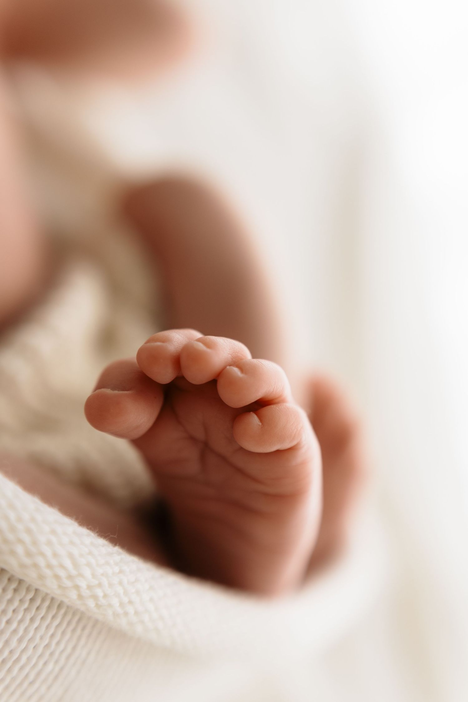 Close-up of a newborn baby's tiny toes and foot wrapped in a soft white knit blanket.