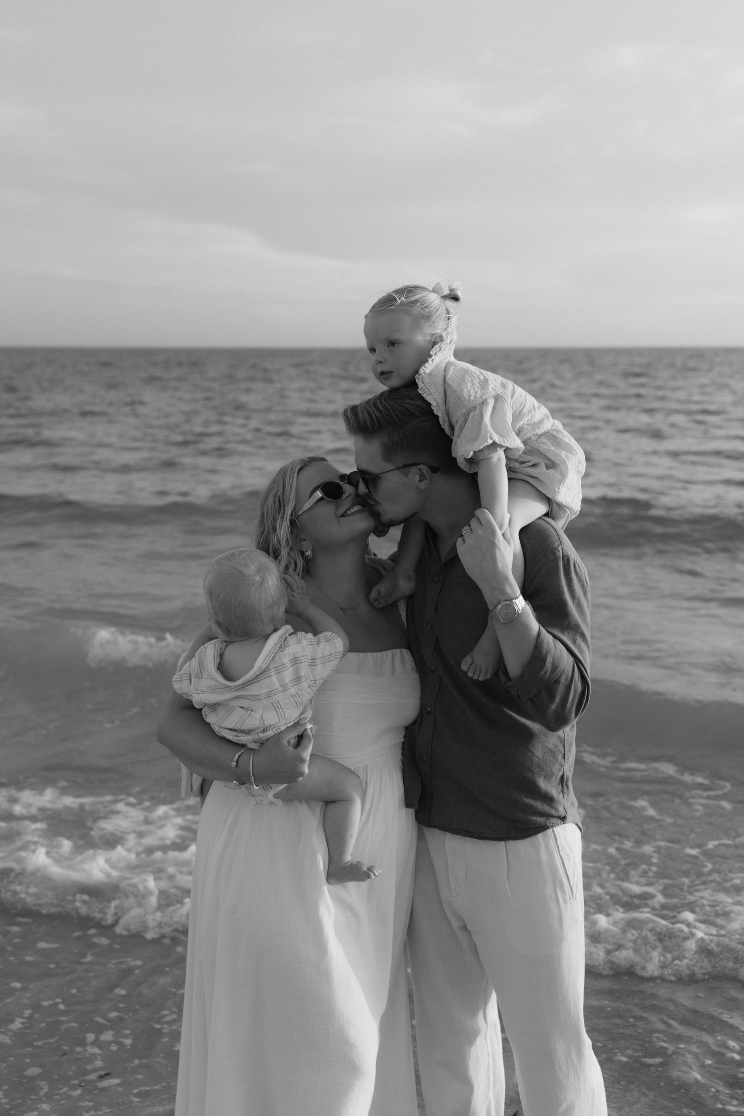 A tender family moment captured in black and white on a beach with crashing waves.
