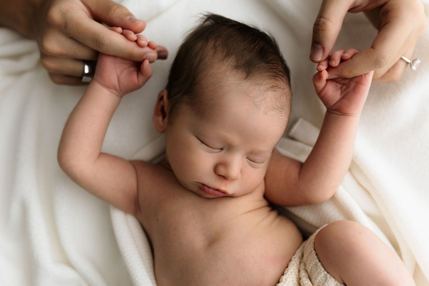 Peaceful sleeping newborn baby held by parents hands on a soft white blanket in a serene newborn photography session.