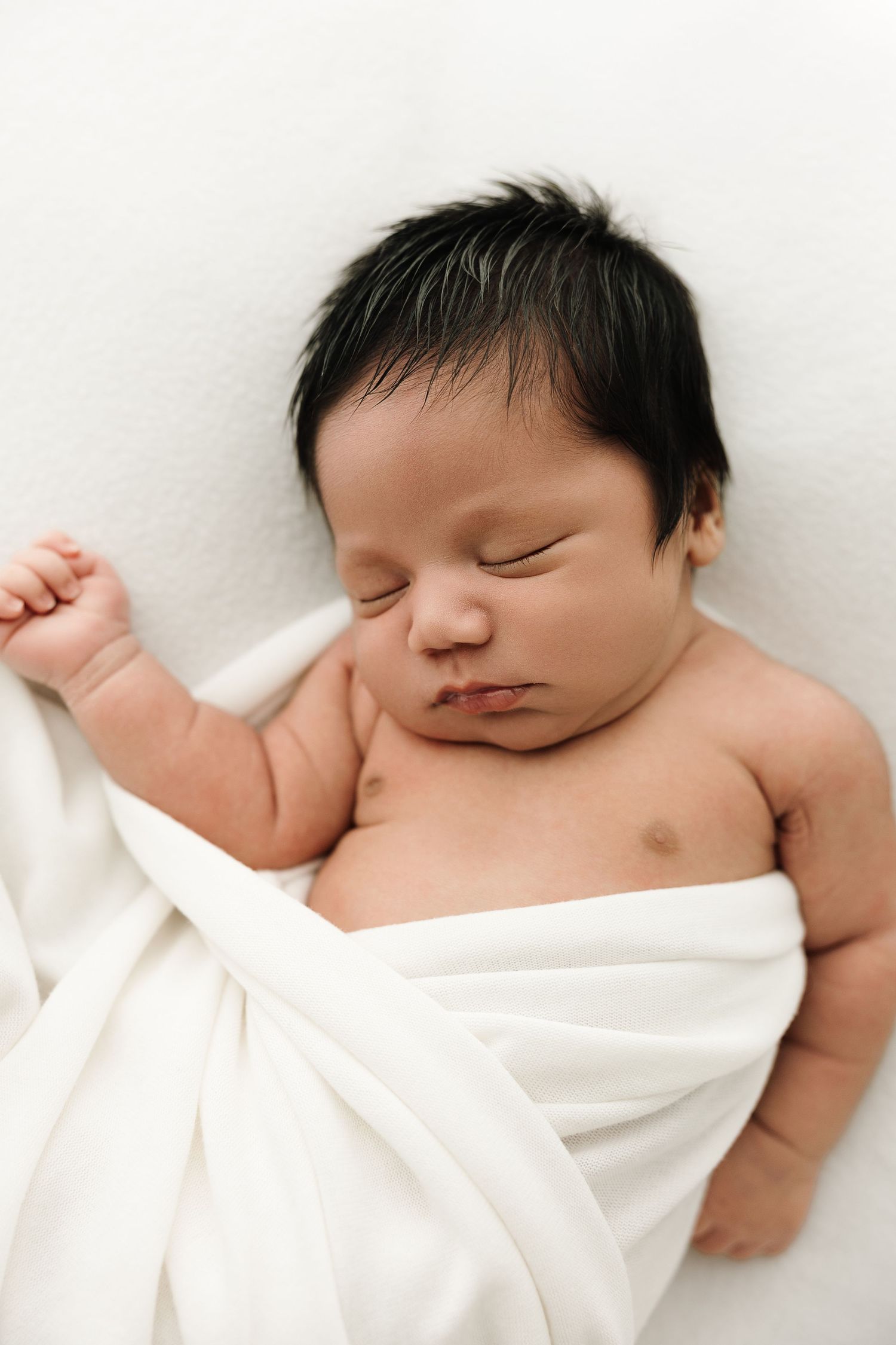 Sleeping newborn baby wrapped in soft white blanket against white background.