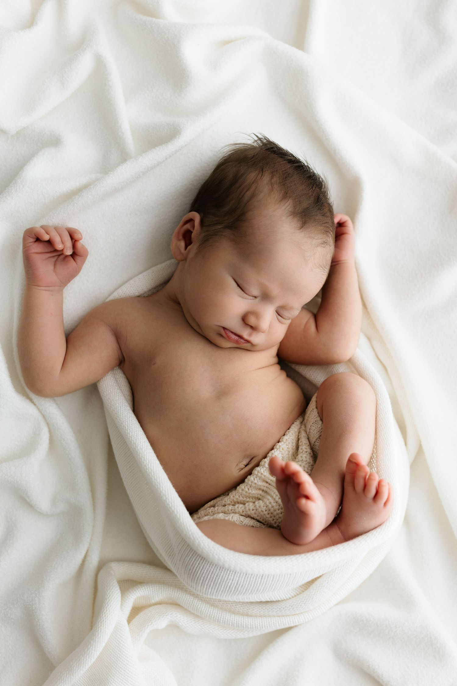 Peaceful newborn baby sleeping wrapped in a white knit blanket on a soft white background.
