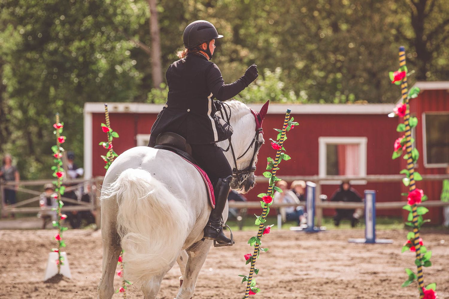 Equestrian arena with red building and colorful decorative poles during a competition.