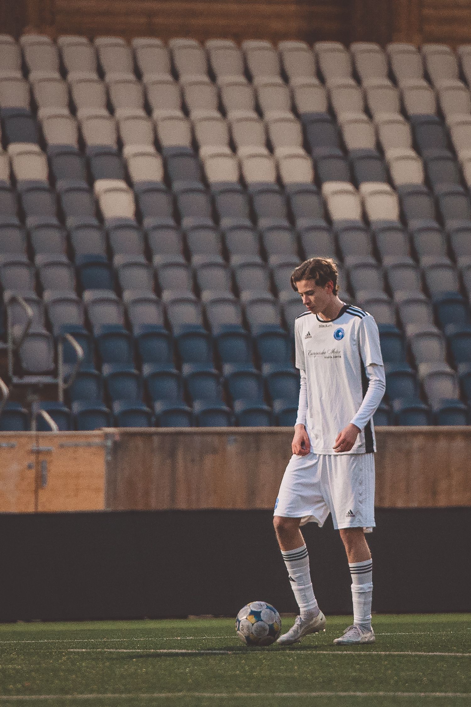 Soccer player in white uniform stands alone on field looking downward during match.