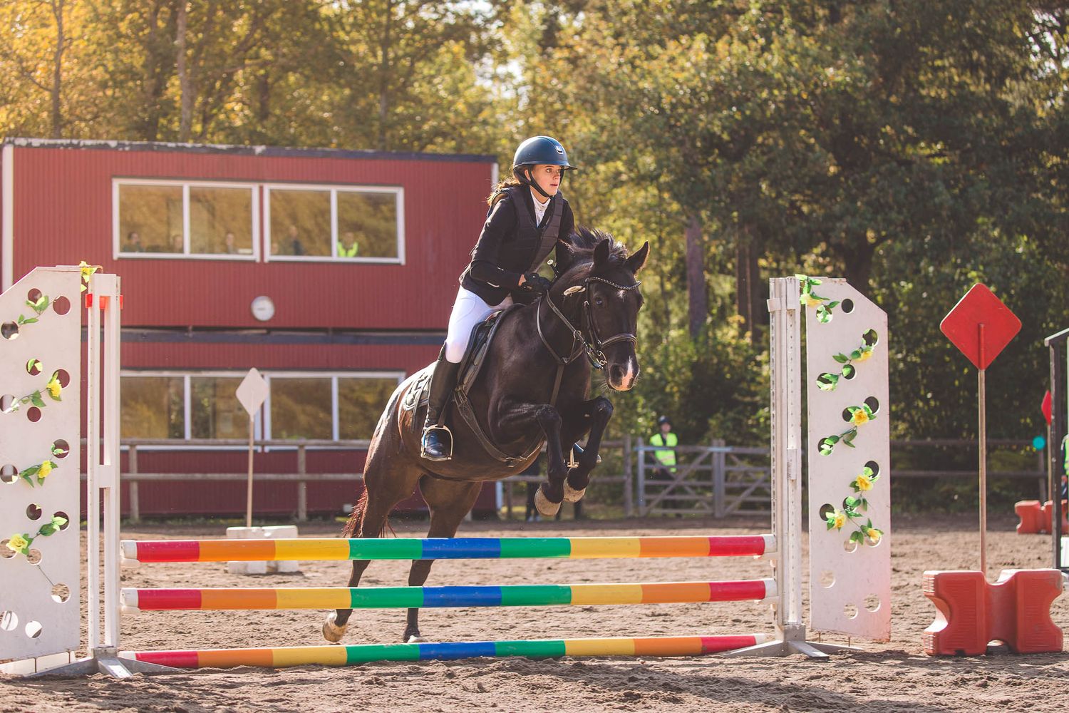 Horse and rider perform dressage movements in front of a red building with decorative elements.