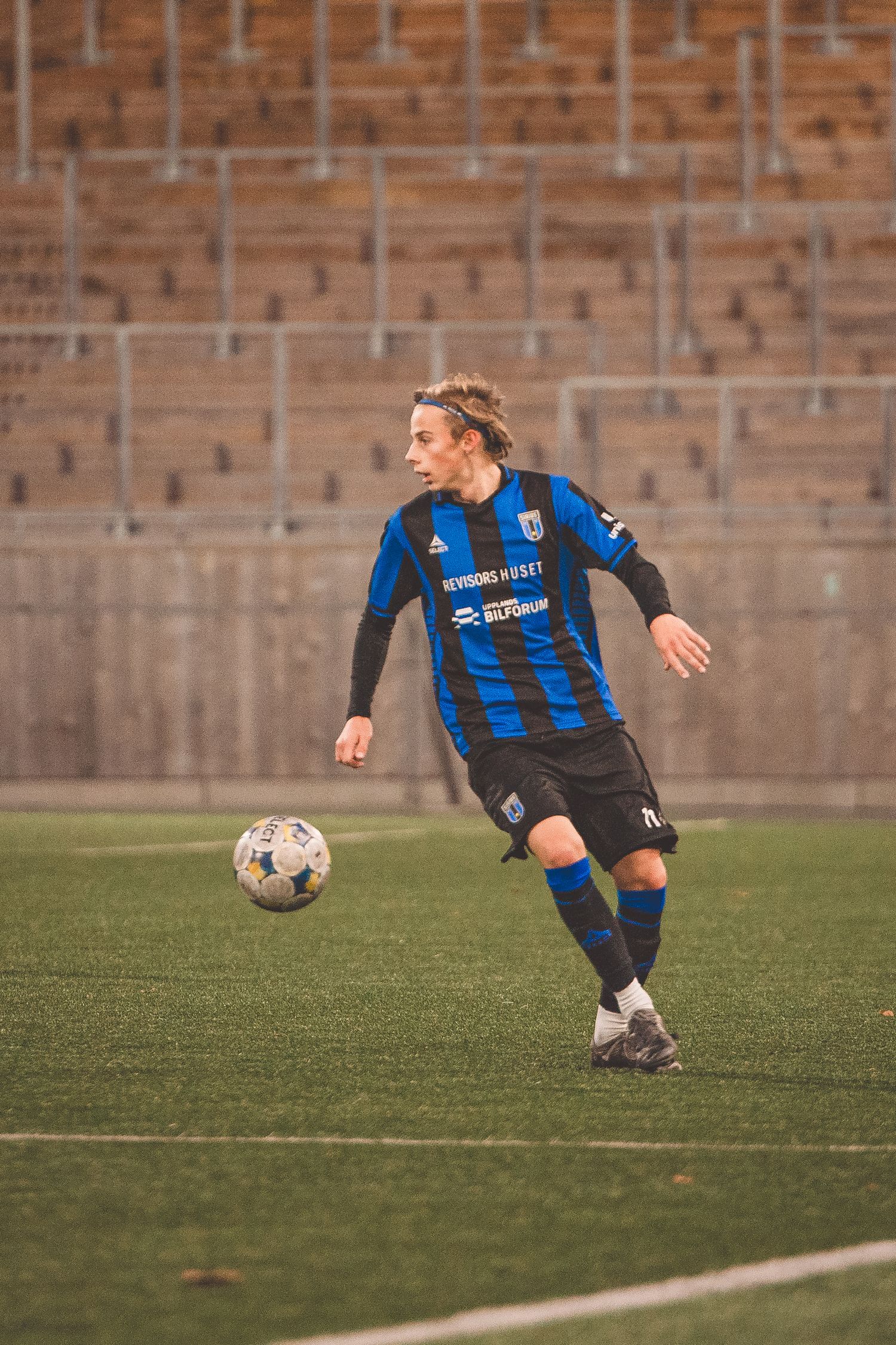 Soccer player in blue and black striped uniform dribbles the ball across the field.