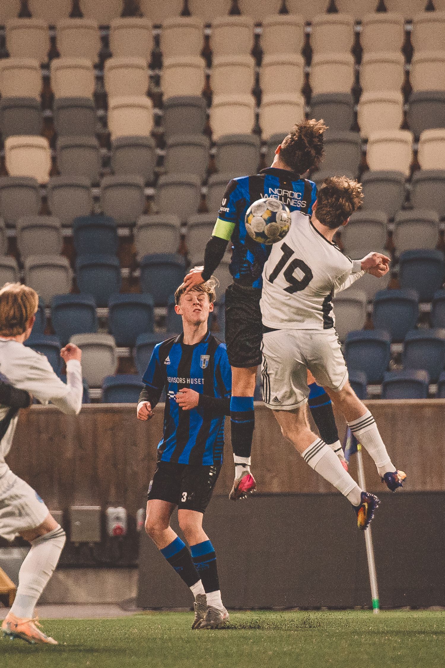Soccer players from opposing teams jump high to contest a header during a match.