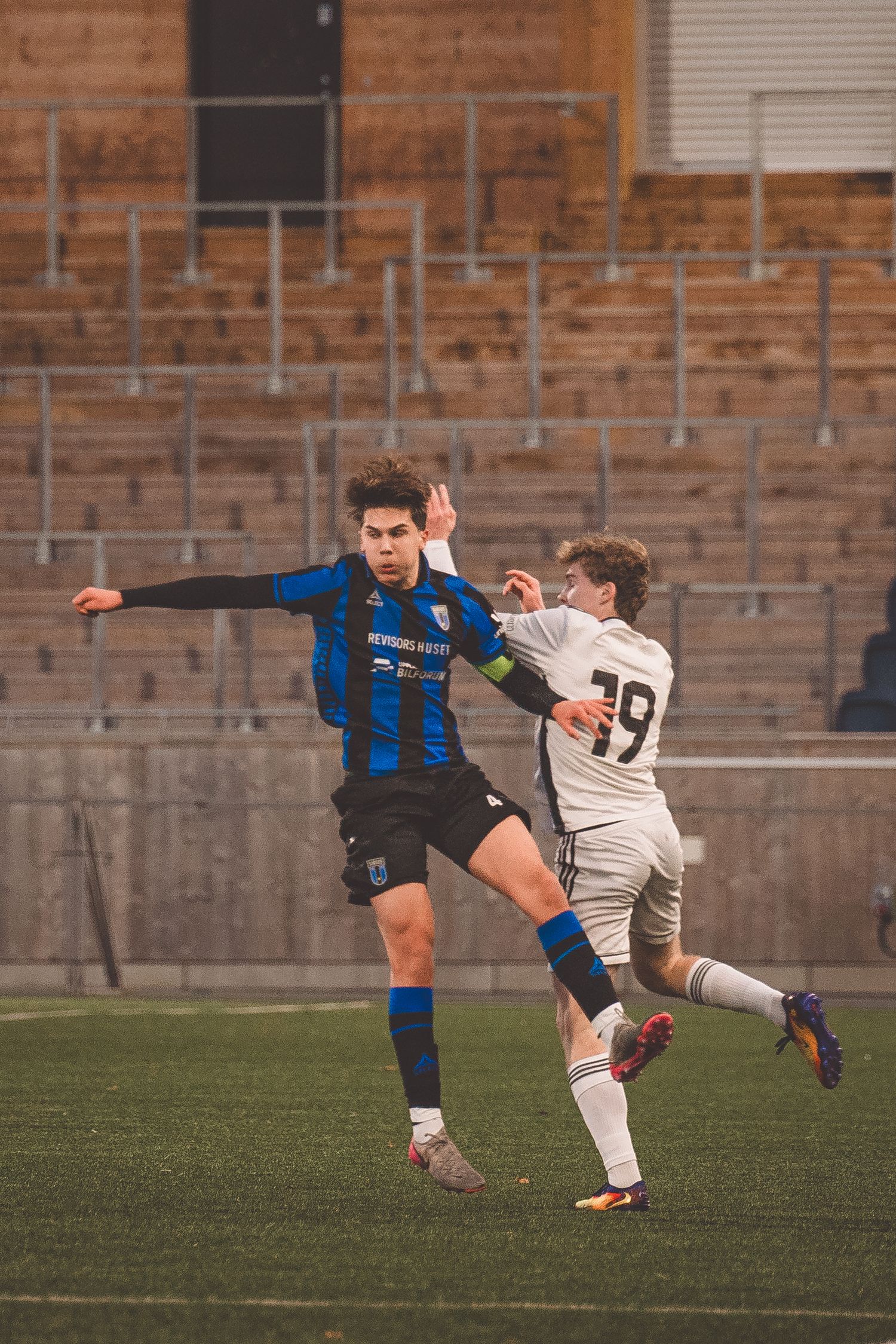 Soccer players in blue and white uniforms compete for the ball during an intense match on a grass field.