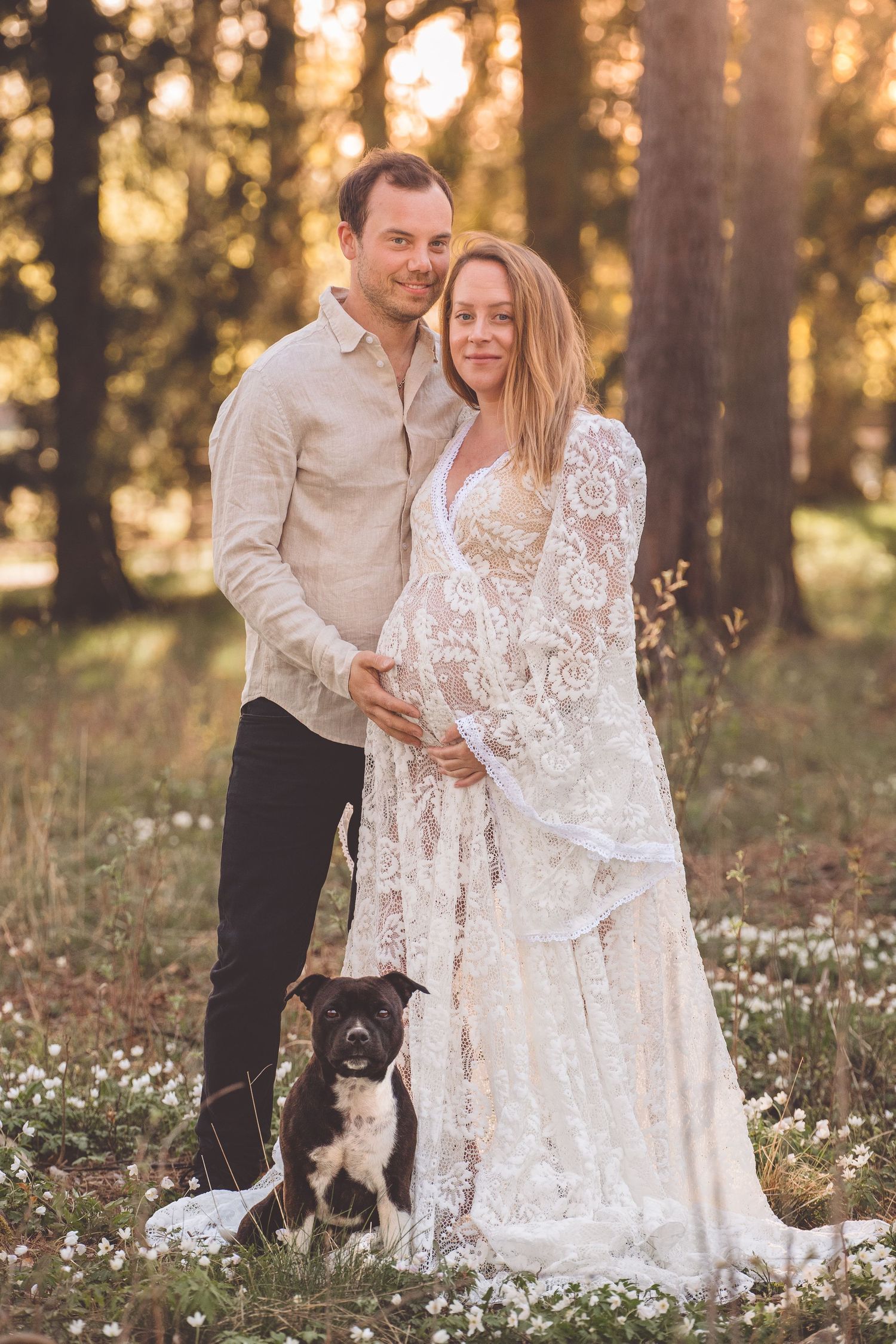 A couple in romantic sunset forest setting with their black dog surrounded by wildflowers.