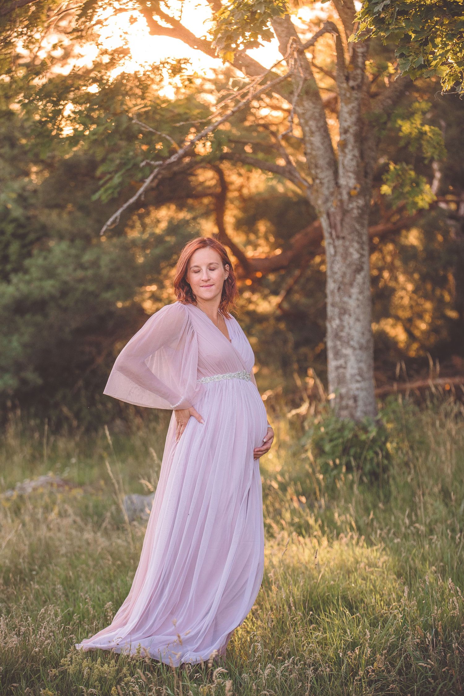 A person in a flowing pink dress poses gracefully in a sunlit meadow during golden hour.