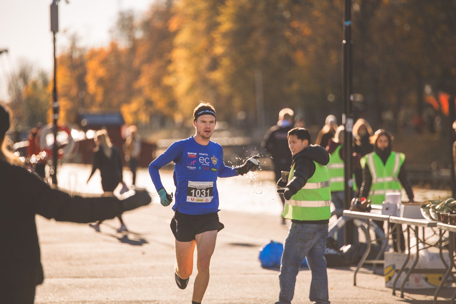 Marathon participants running through a park during an autumn race event.