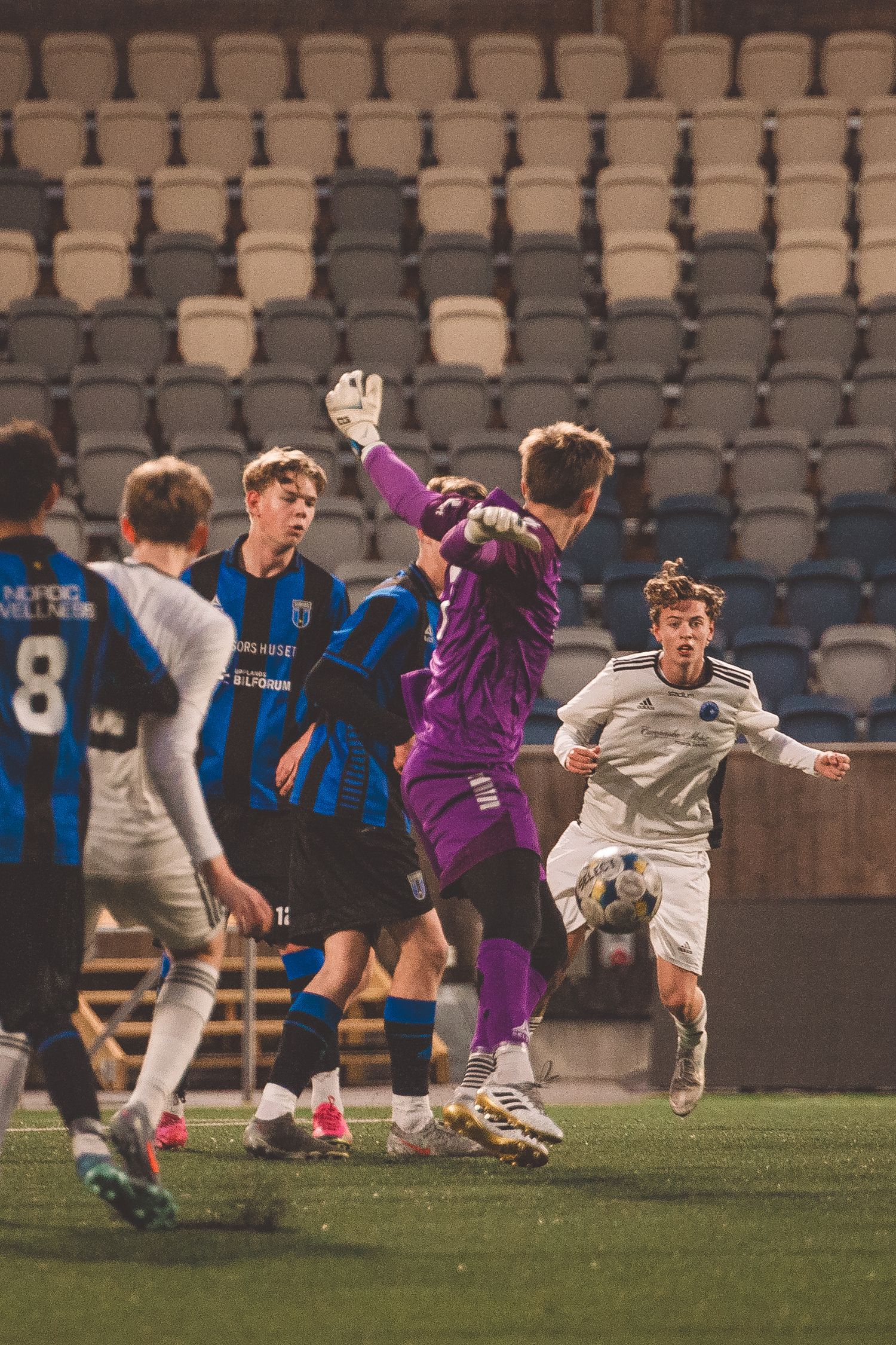 Players leap and dive during a dramatic soccer match with stadium seating in the background.