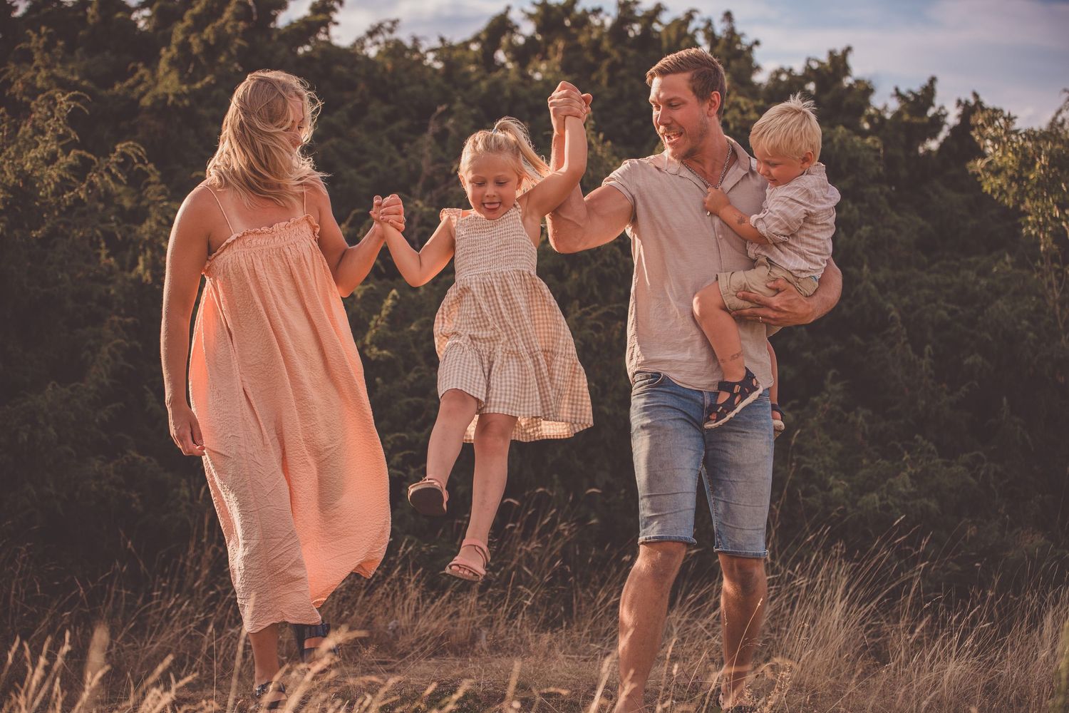 Family members walk and play together in a grassy field during golden hour sunset.