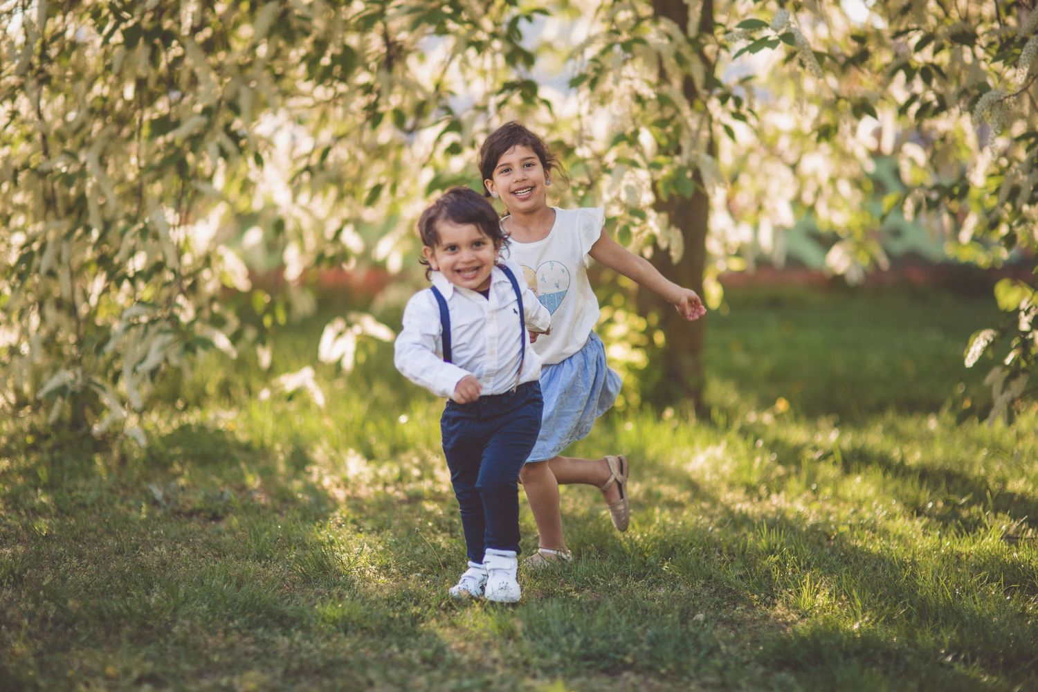 A family enjoys a playful moment together on green grass under dappled sunlight in a park setting.