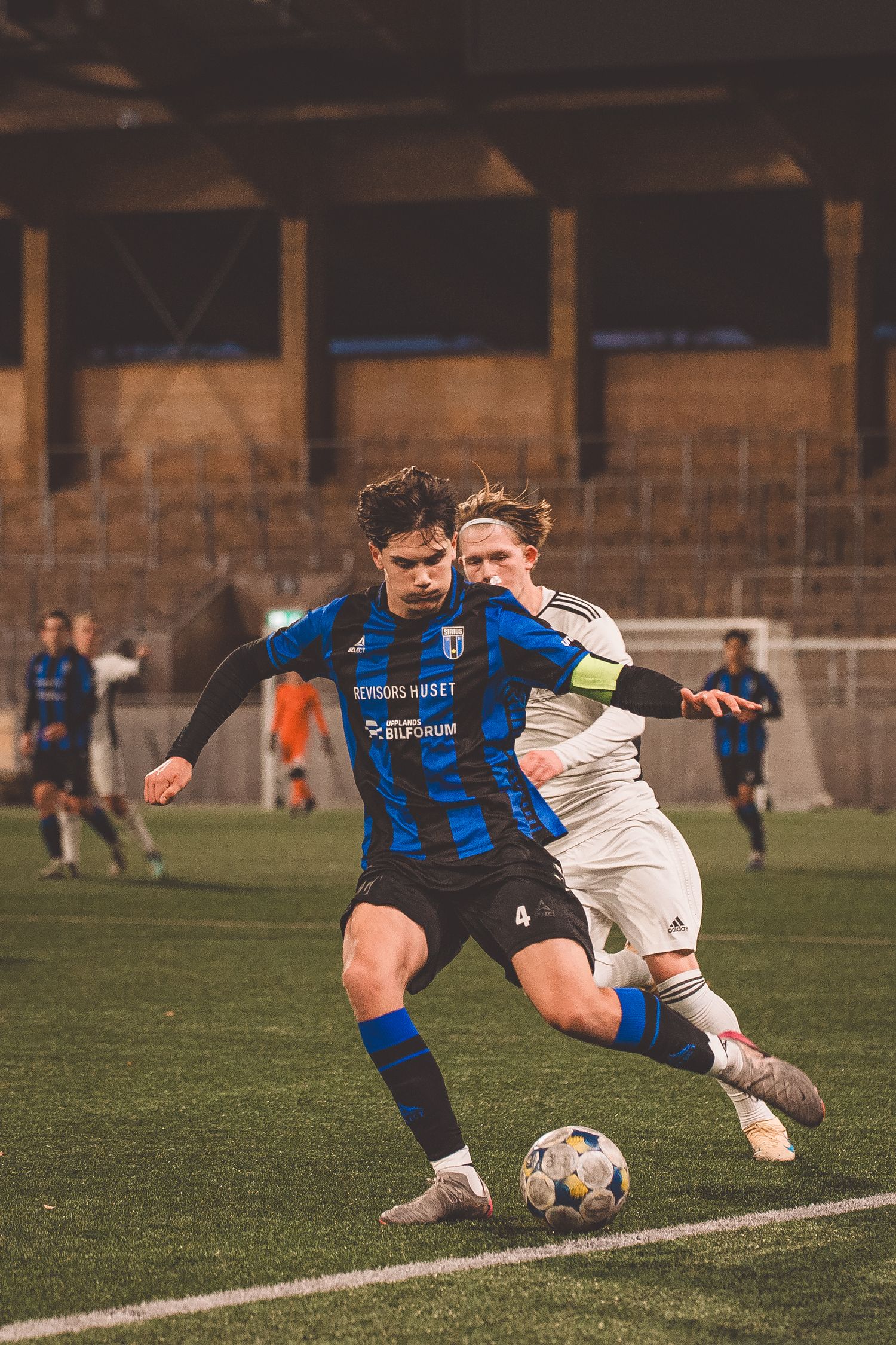 Two soccer players battle for possession of the ball near the sideline during a competitive match.